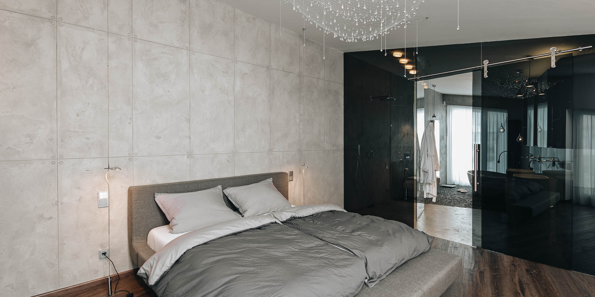 Ložnice interiéru vily s pohledovým betonem, křišťálovým svítidlem a koupelnou za kouřovým sklem, OOOOX