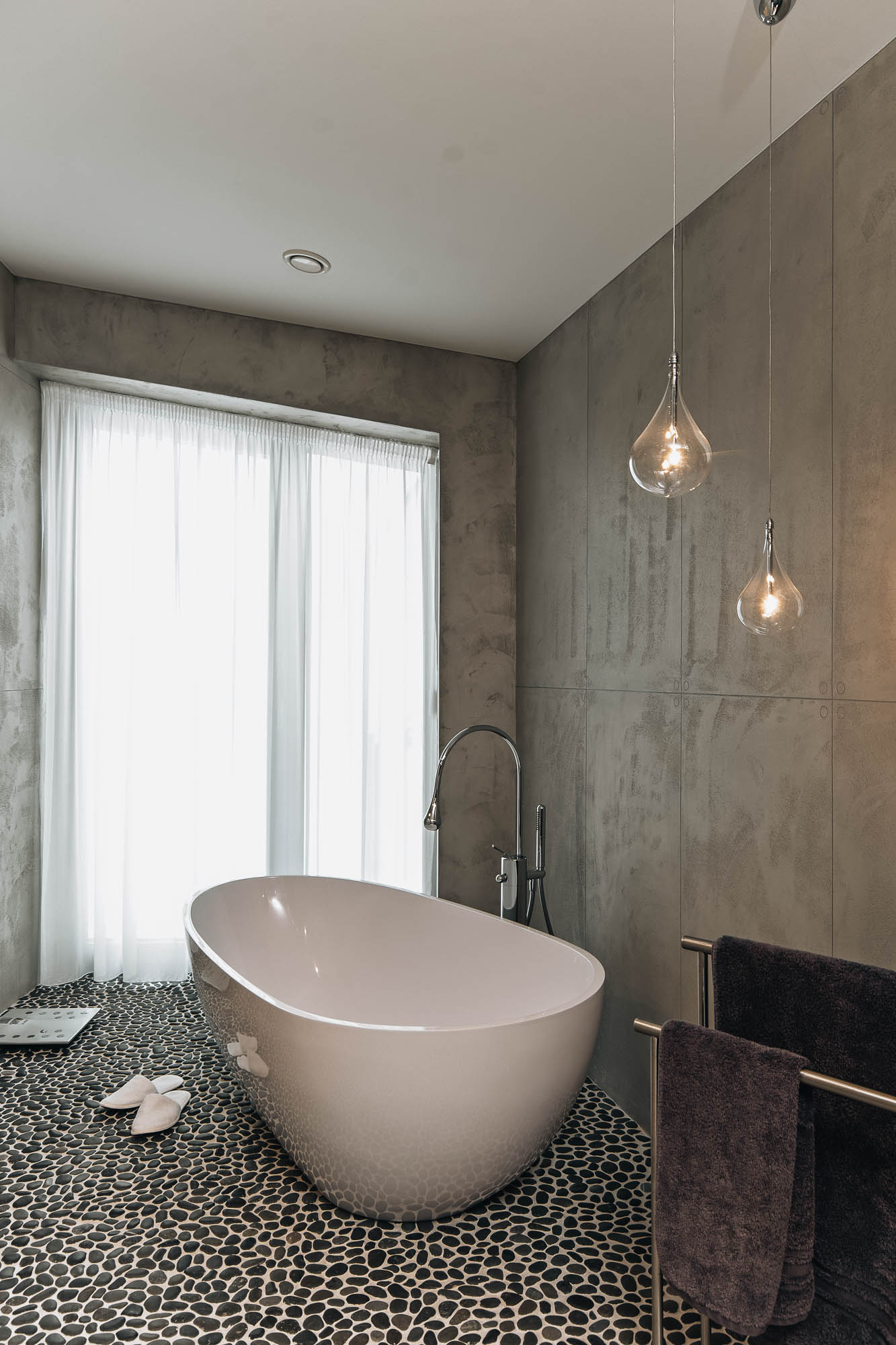 Volně stojící oválná vana na oblázkovém dlaždičkování ve velkorysé koupelně interiéru vily, návrh OOOOX