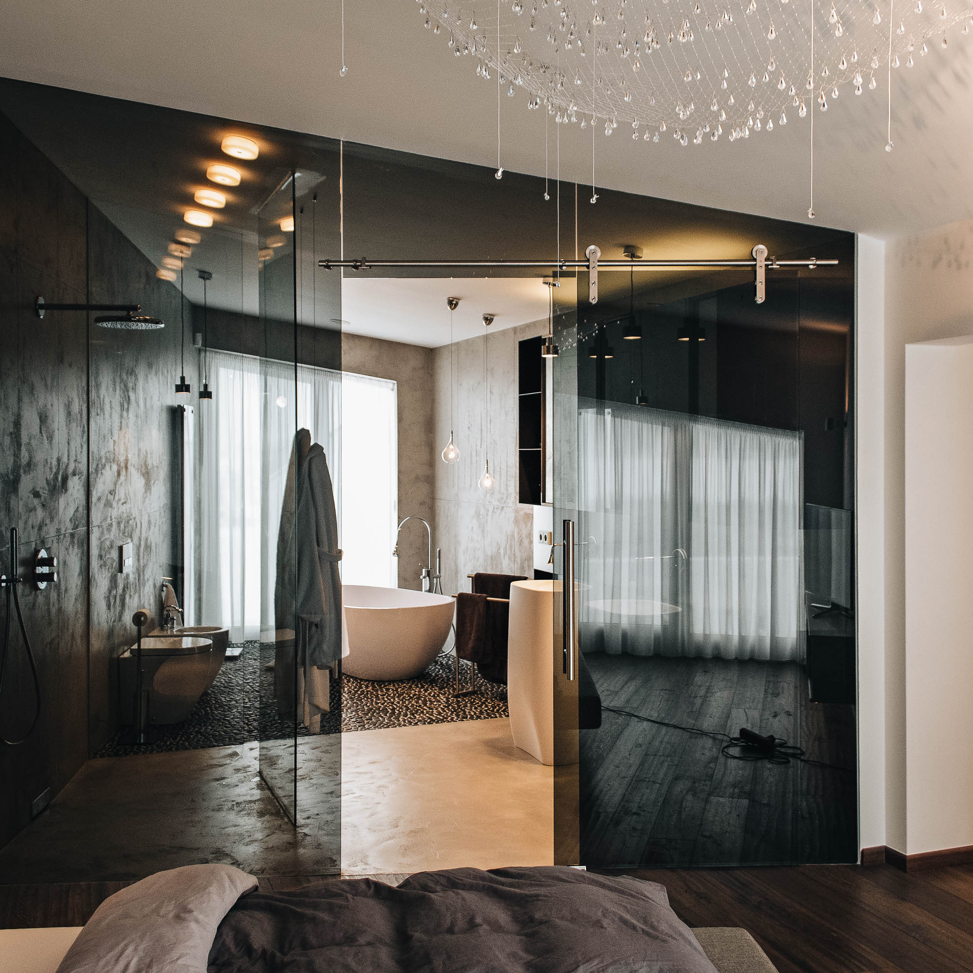 Ložnice vily s kouřovým sklem oddělujícím koupelnu, křišťálovým svítidlem a čalouněnou postelí, OOOOX