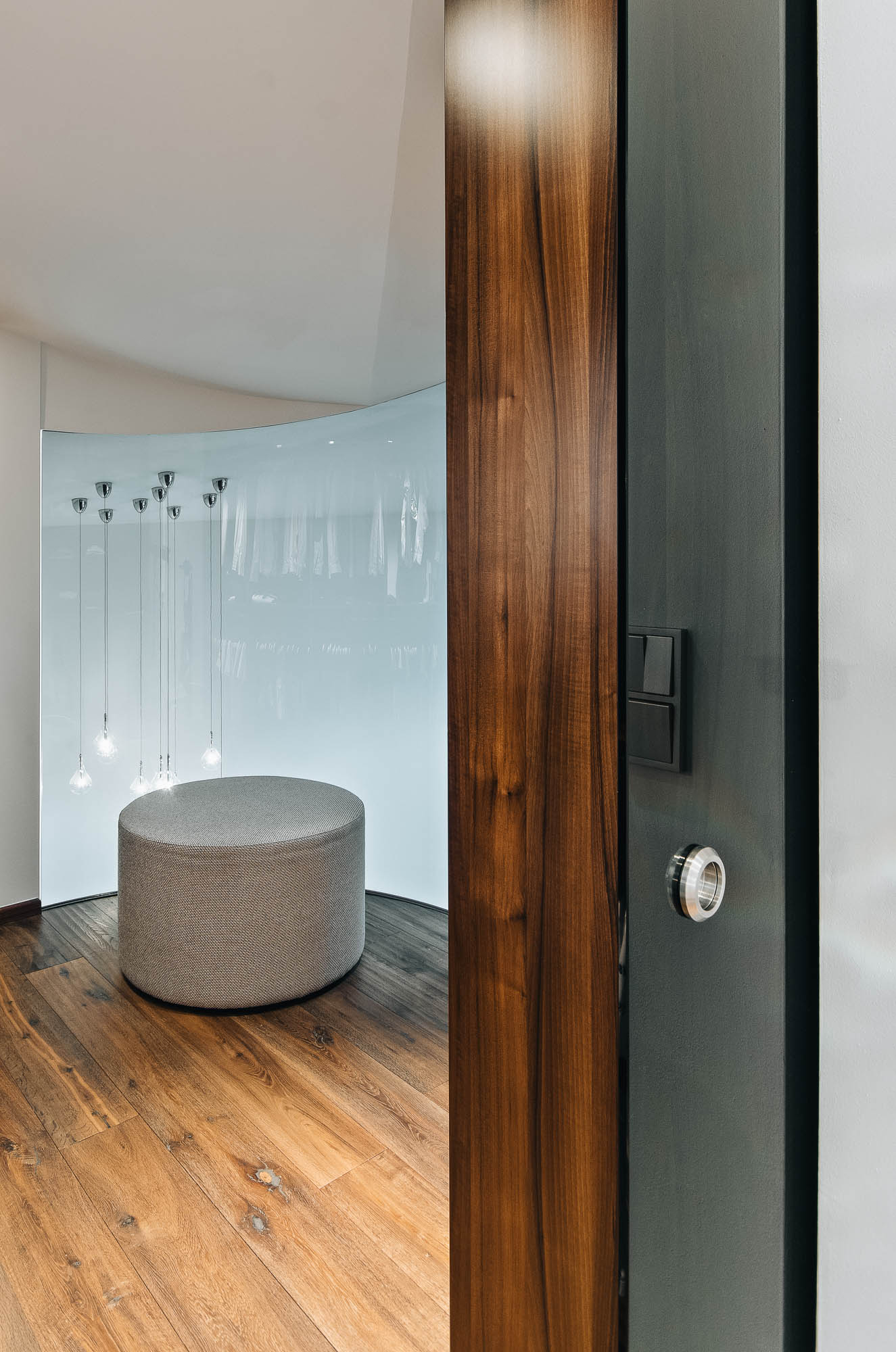 Vstup do šatny v patře vily s oblým kouřovým sklem, designovým osvětlením a interiérem OOOOX