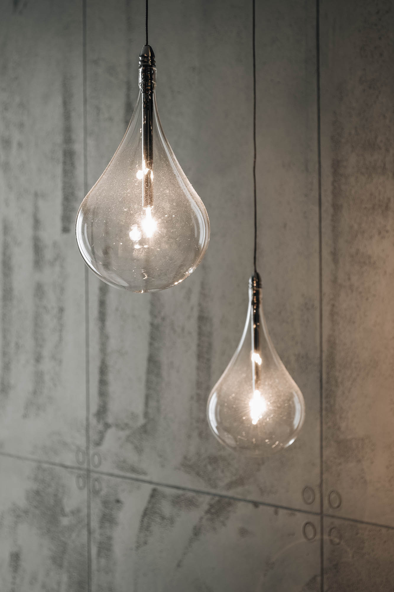 Skleněná závěsná svítidla ve tvaru kapky na pozadí pohledového betonového panelu v ložnici vily