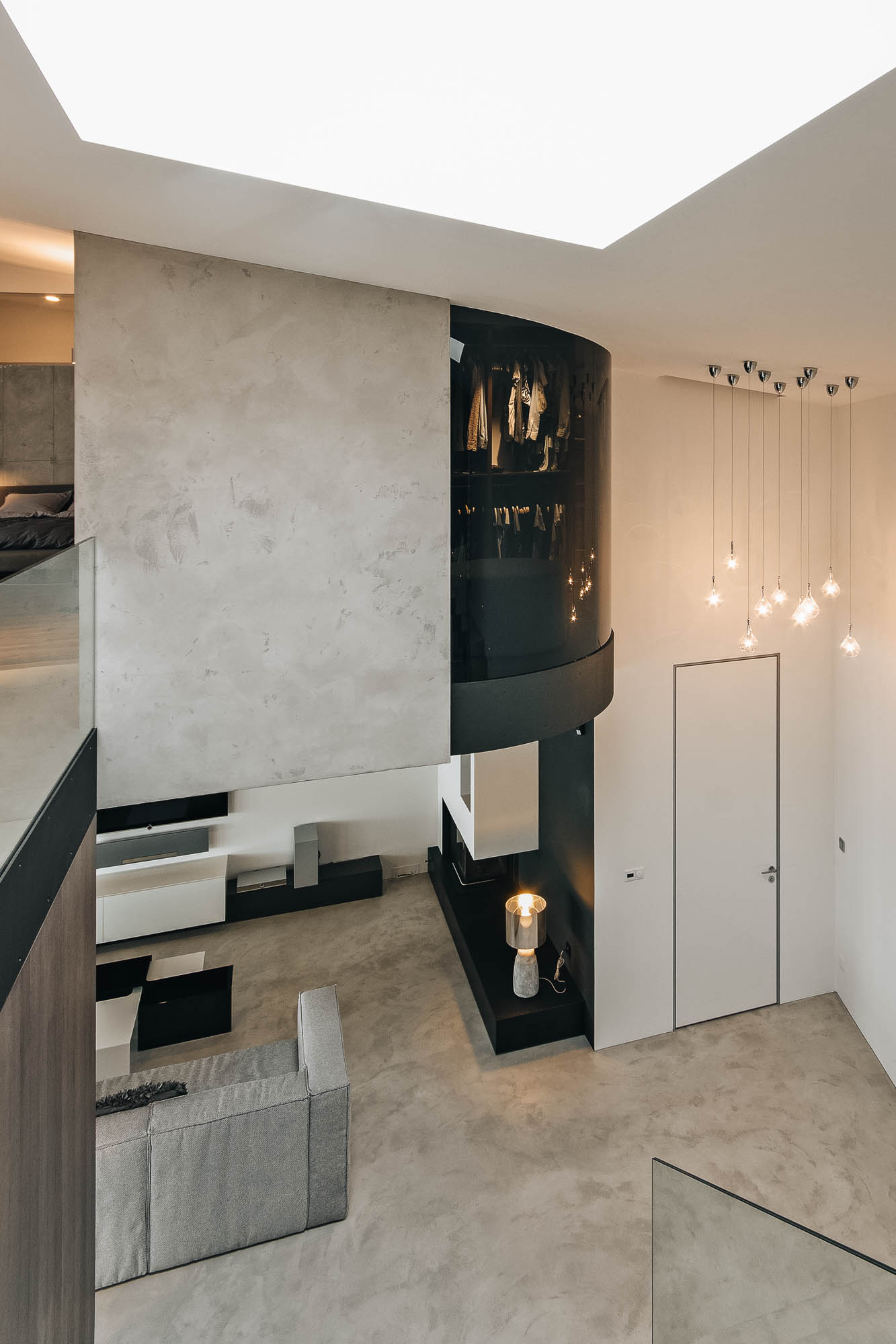 Pohled z patra vily na kulatou šatnu s kouřovým sklem, obývací pokoj a pohledový beton, návrh OOOOX