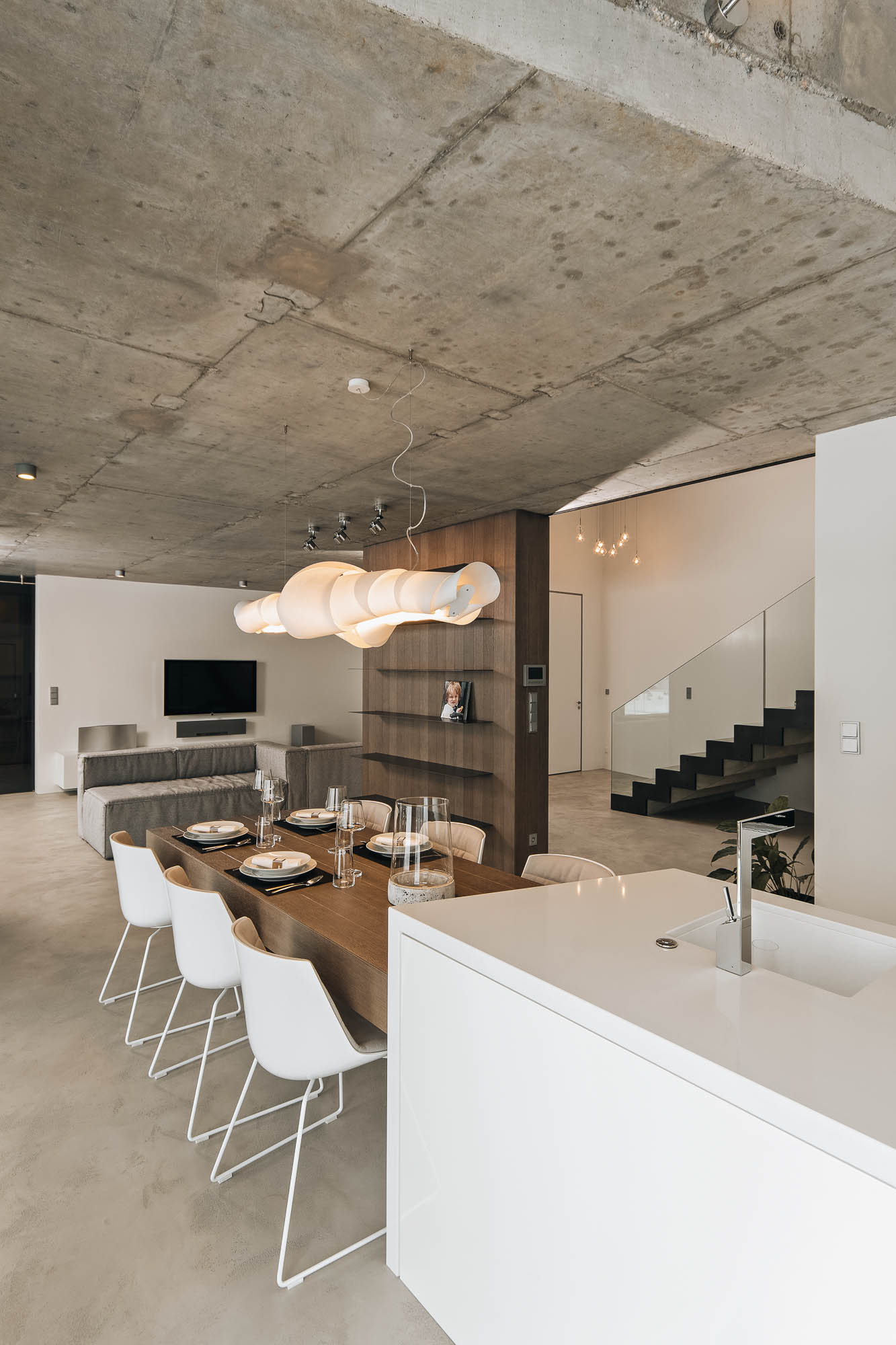 Villa open plan from kitchen island – dining area, living room and staircase with exposed concrete ceiling