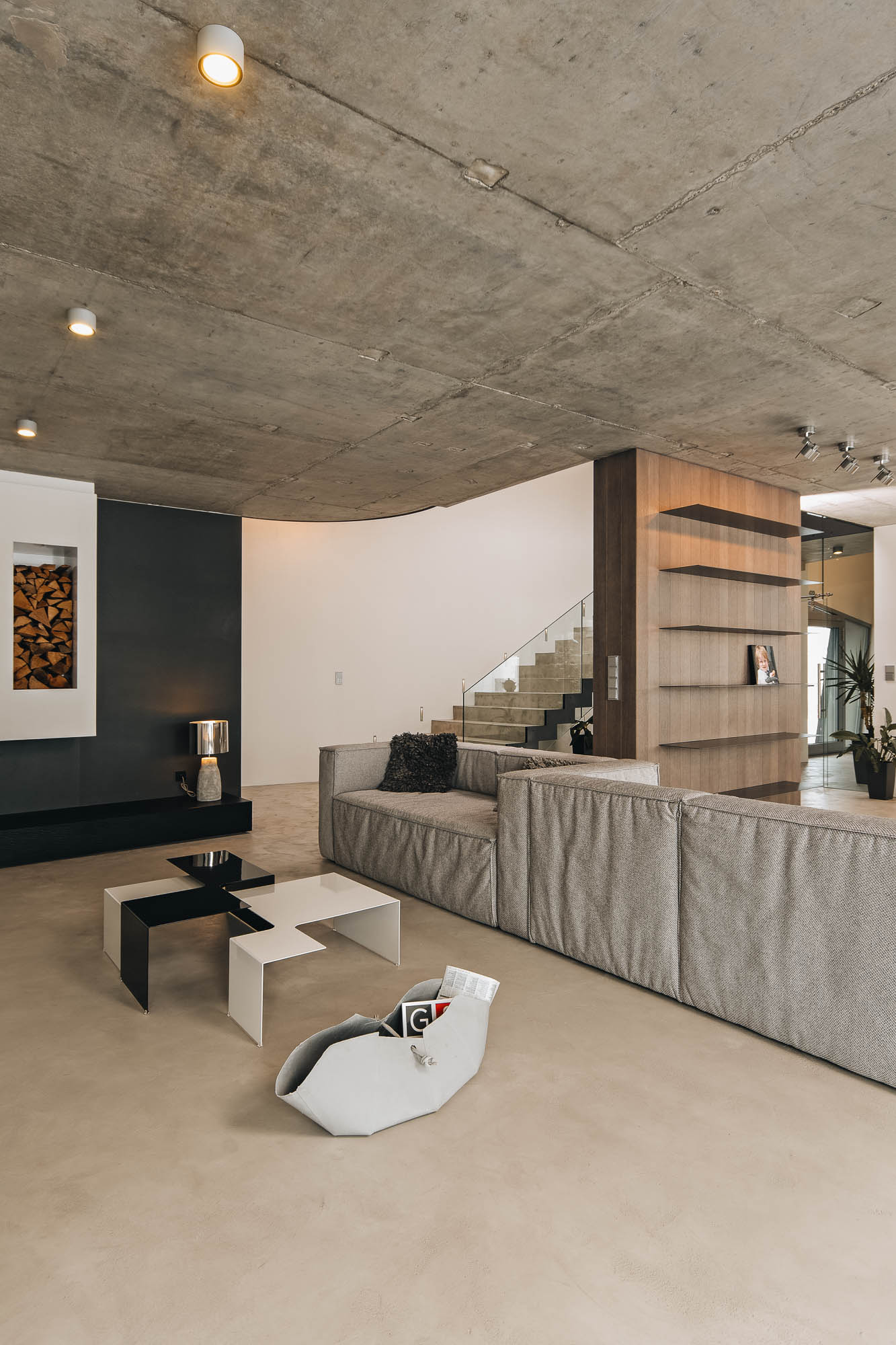 Obývací pokoj vily s pohledovým betonem, krbem s výklenkem na dřevo a geometrickými konferenčními stolky