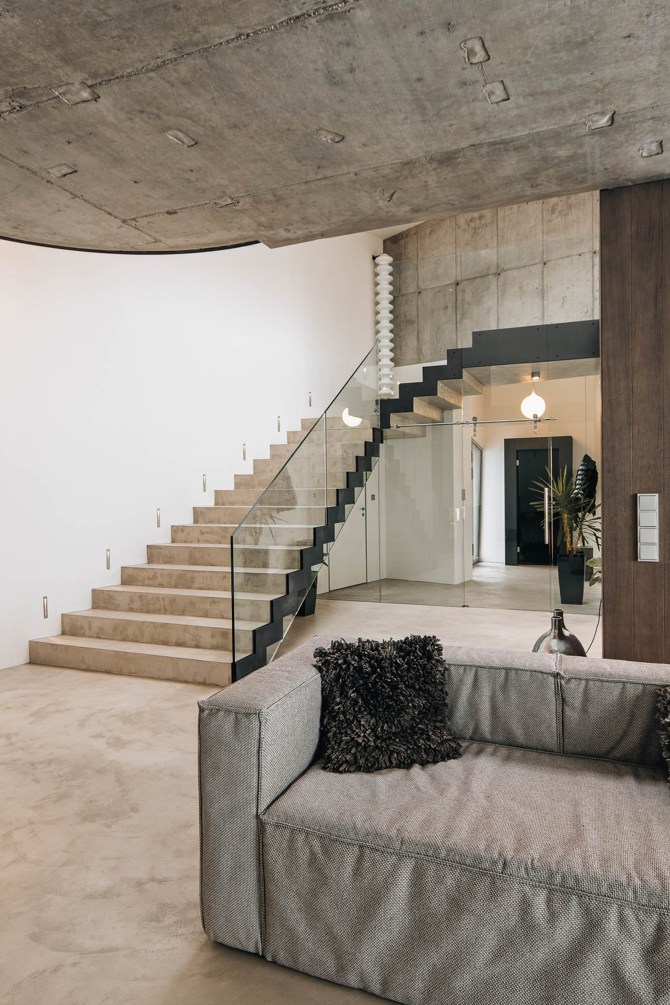Betonové schodiště s skleněným zábradlím a obývací pokoj v interiéru vily s pohledovým betonem, OOOOX