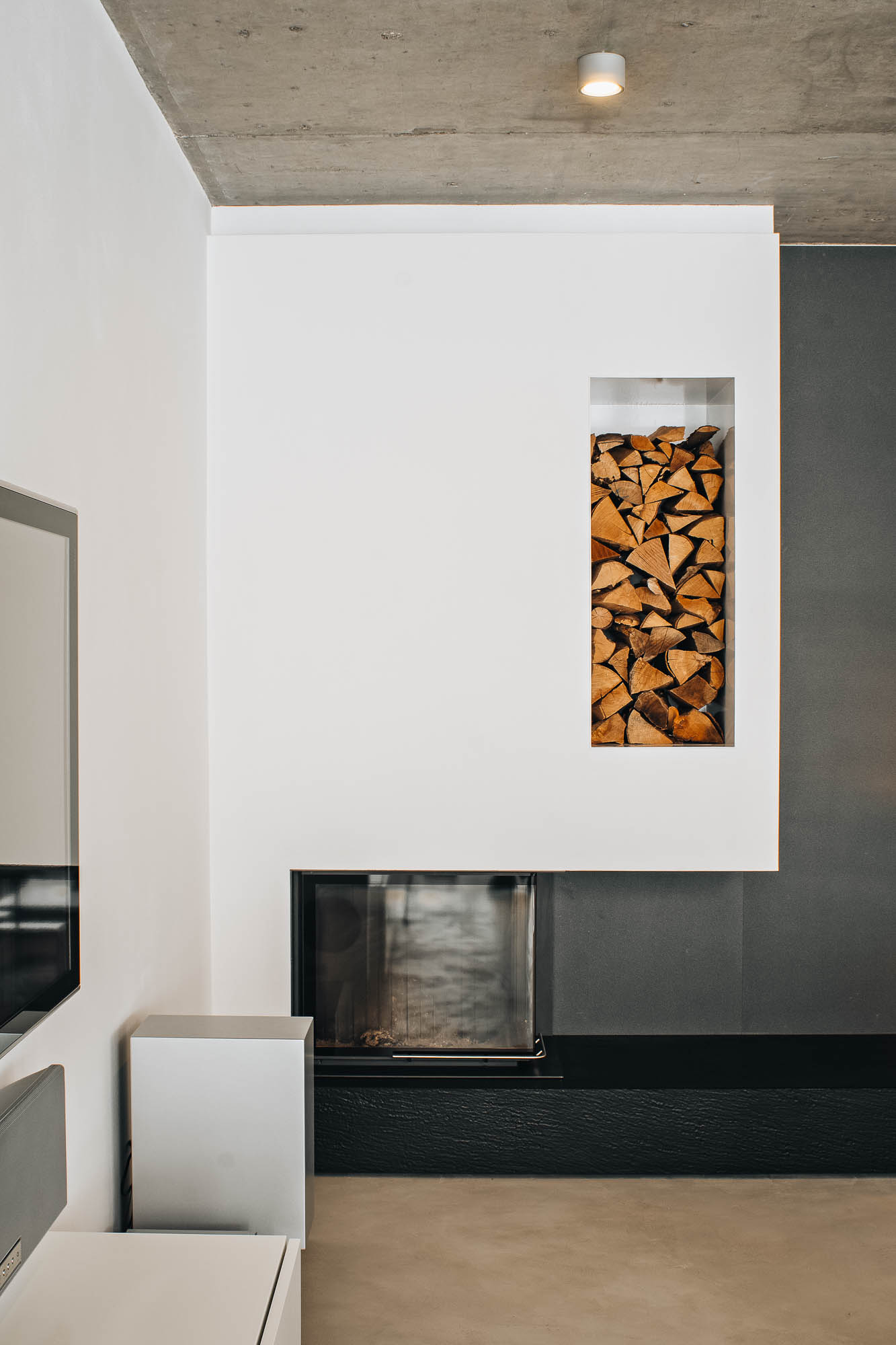 Detail vestavěného krbu s výklenkem na palivové dřevo v obývacím pokoji vily s pohledovým betonem