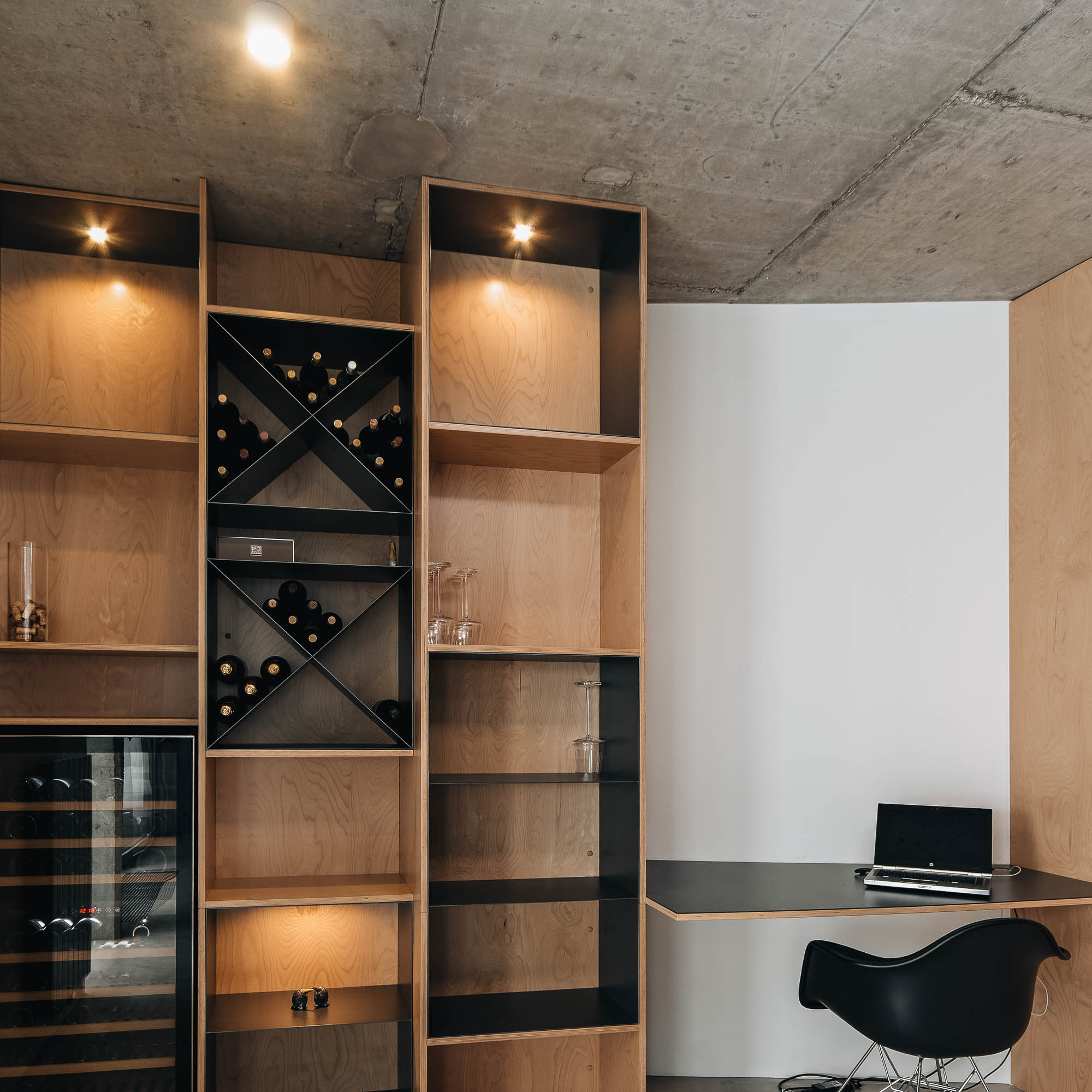 Detail překližkových polic s křížovým úložištěm na víno a černou pracovní deskou v kuřárně vily