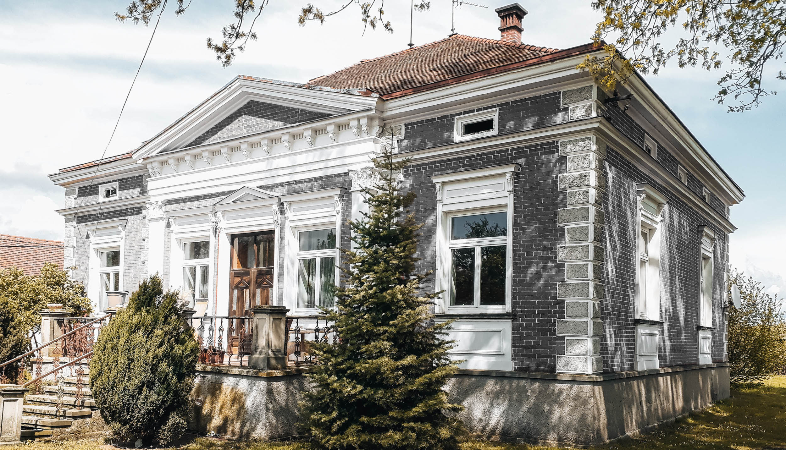Pohled z rohu na historickou cihlovou vilu s klasicistním průčelím a zahradou, stav před rekonstrukcí. OOOOX
