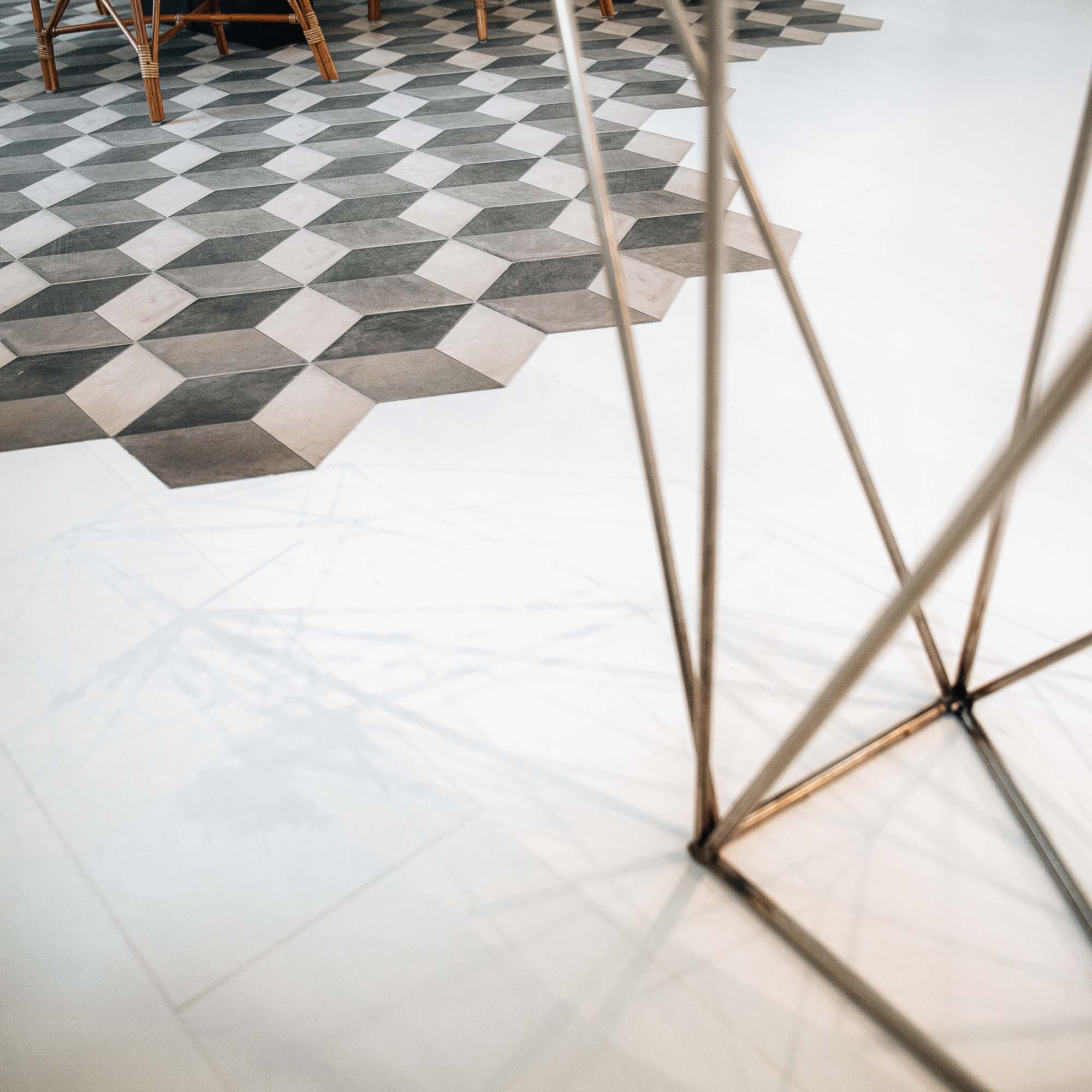 Detail přechodu podlah v bytě Pařížská – geometrická hexagonální mozaika plynule přechází do bílé mramorové dlažby, v popředí mosasné trojúhelníkové nožky stolu