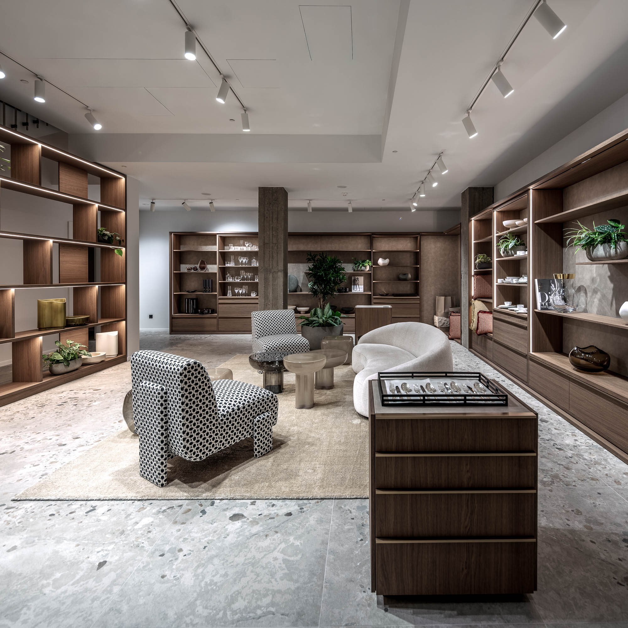 Celkový pohled na suterénní showroom LA TABLE Pařížská s sezénní zónou, vzorovanými křesly a vestavnými policemi s produkty po obvodu prostoru – OOOOX