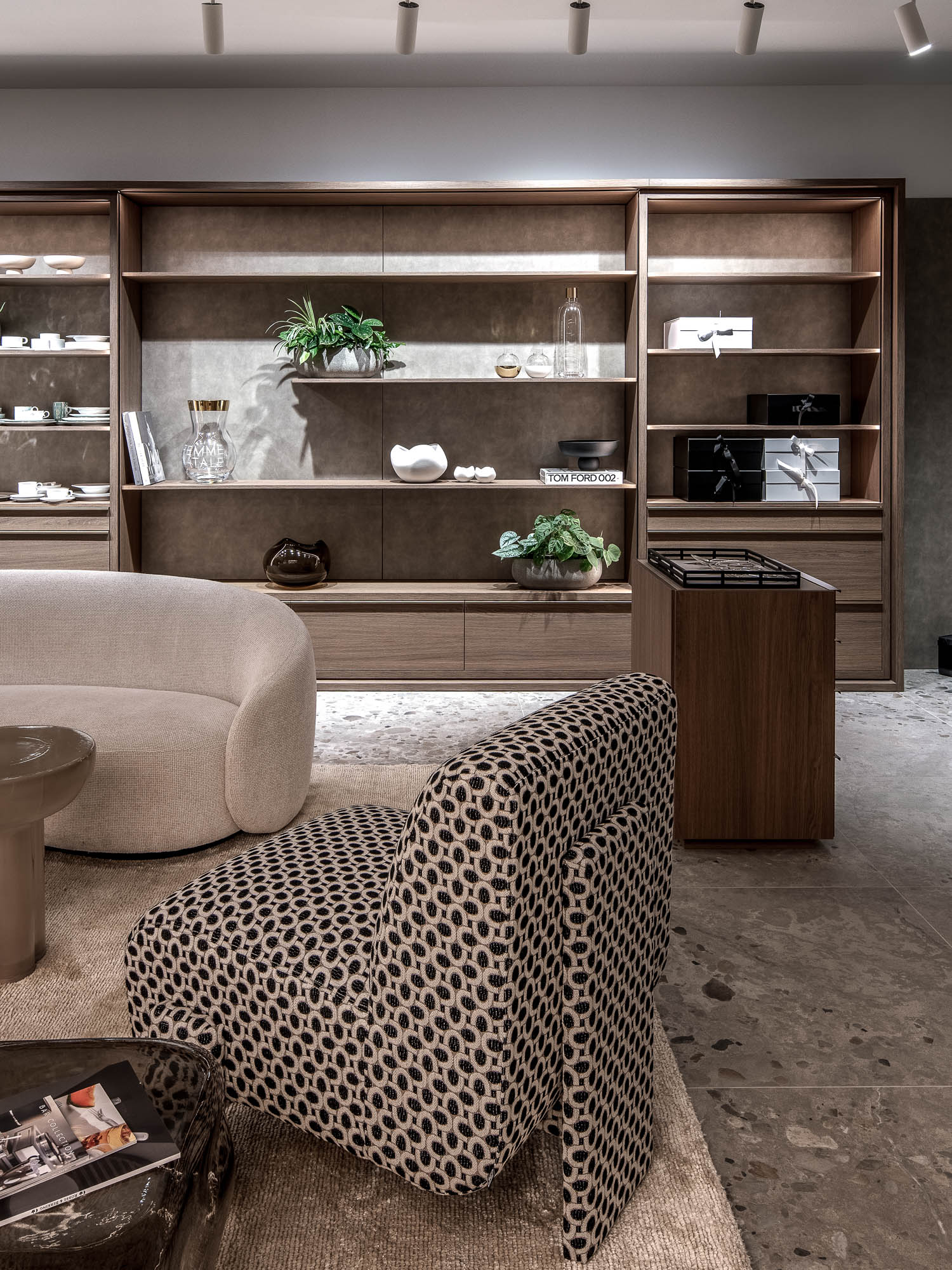 Detail vzorovaného křesla a zaoblené krémové sedačky na koberci před podsvícenými dubovými policemi s luxusním zbožím – showroom LA TABLE Pařížská OOOOX