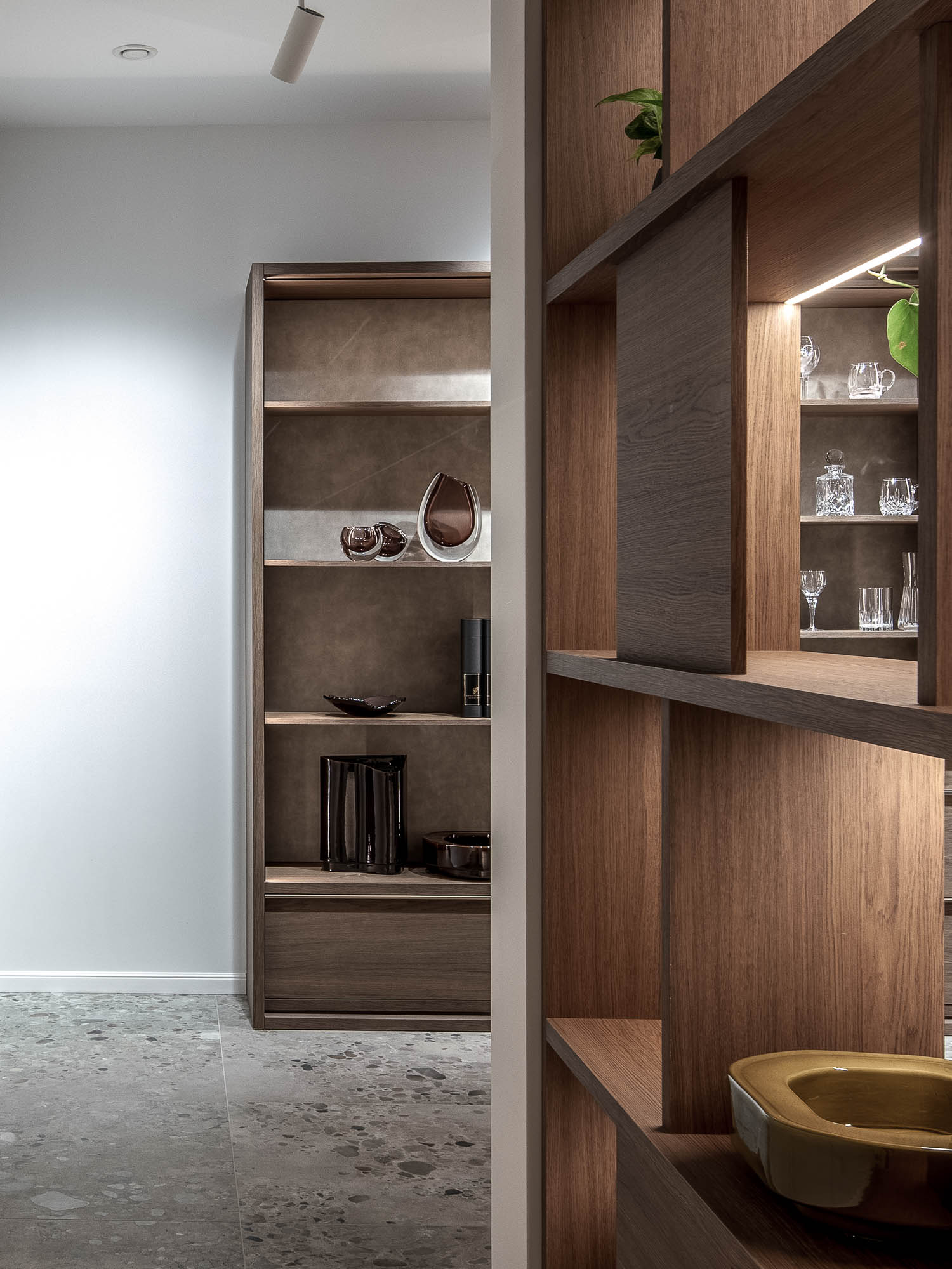 Detail výstavních polic showroomu LA TABLE Pařížská s křišťálovými skleničkami, tmavou keramikou a skleněnými objekty na podsvícených dubových policích – OOOOX