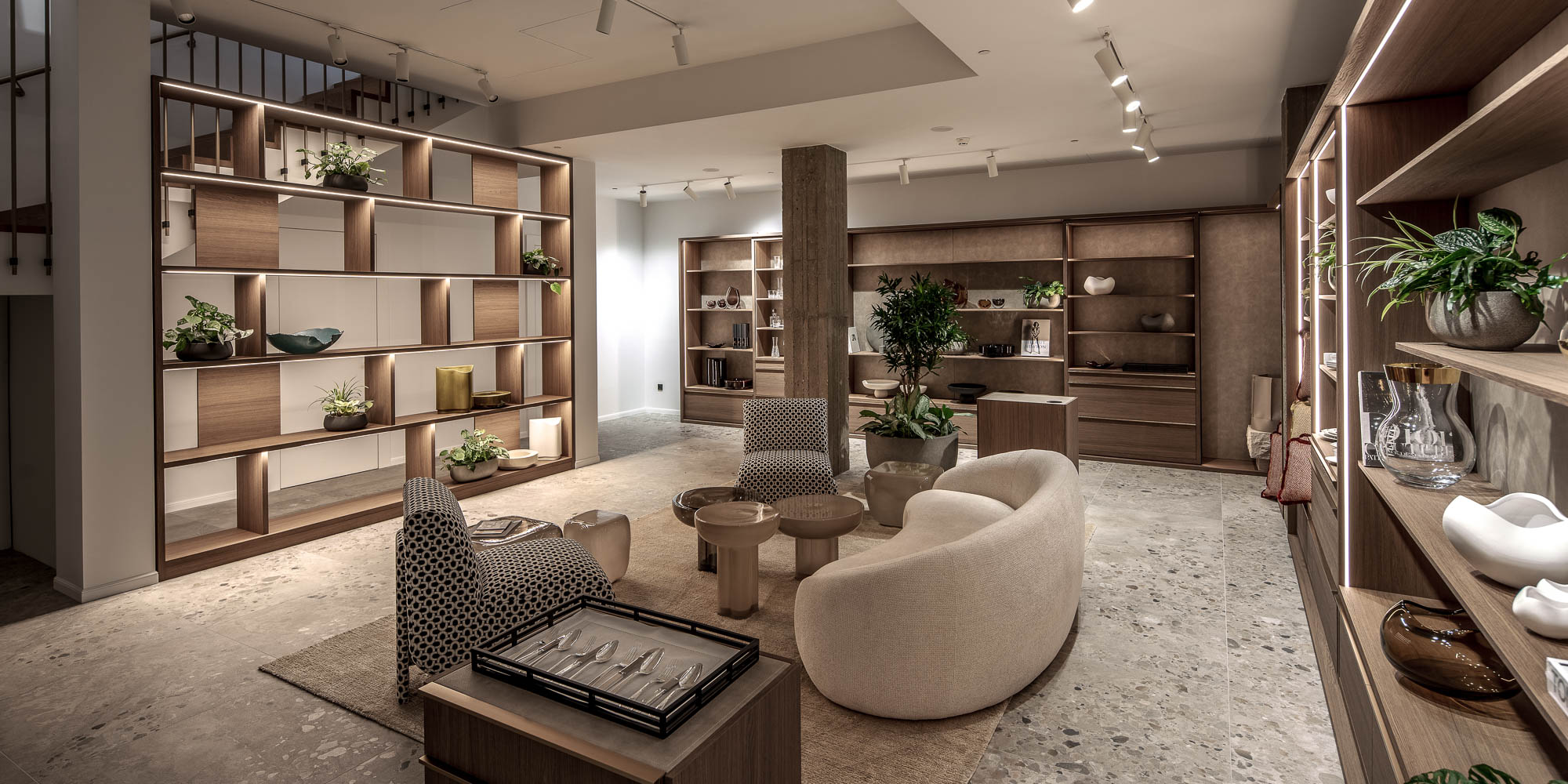 Panoramatický pohled na showroom LA TABLE Pařížská s policovými stěnami, sezénní zónou, přiznaným betonovým sloupem a schodišťovým zábradlím – OOOOX