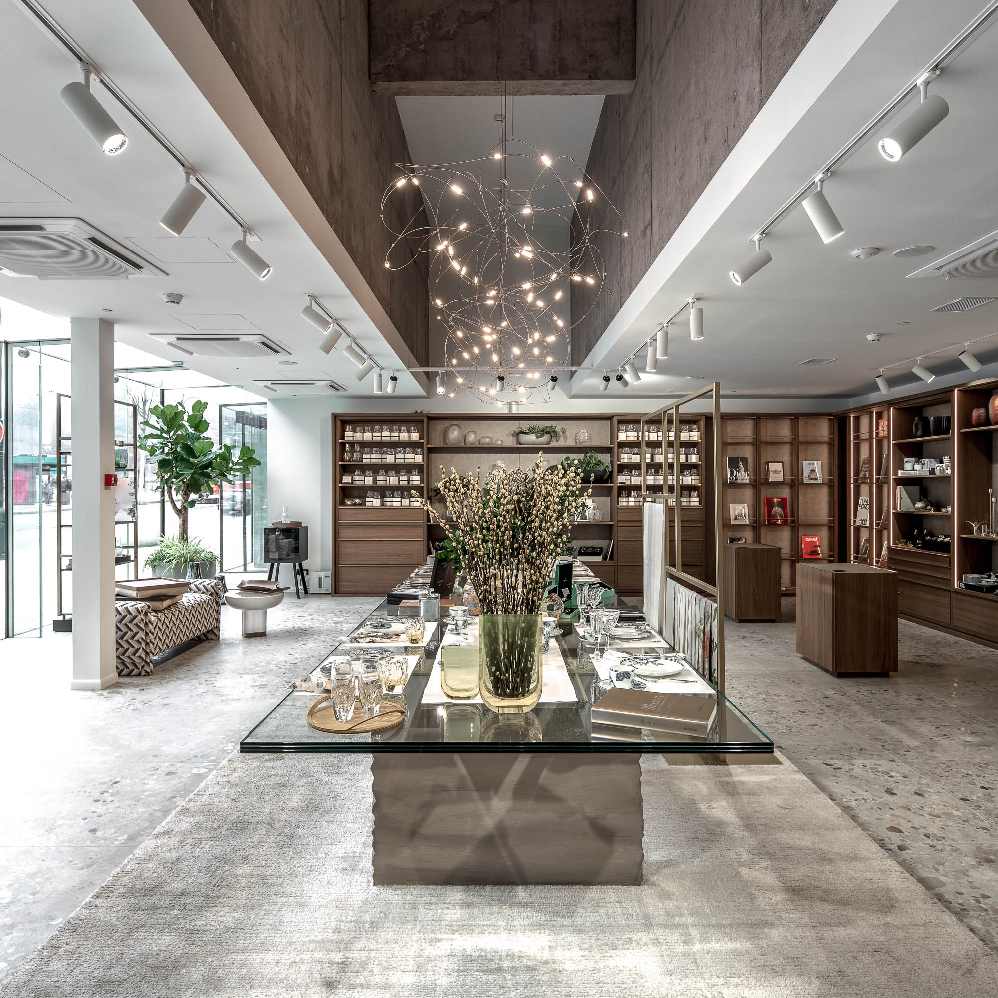 Pohled shora na showroom LA TABLE Pařížská – centrální skleněný stůl s výstavou produktů, svítidlo Moooi Flock of Light a prosklená fasáda do ulice – OOOOX