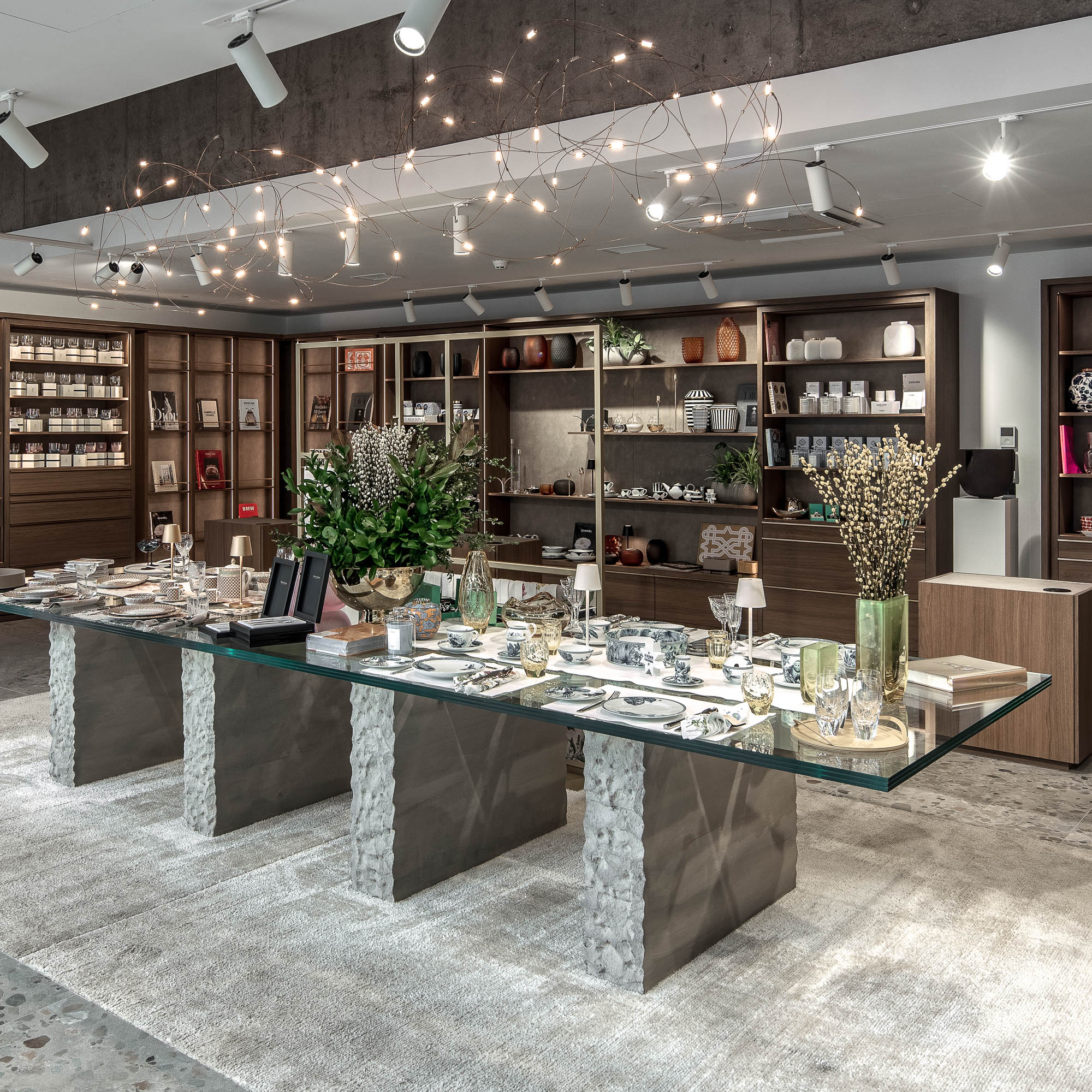 Plně aranžovaný showroom LA TABLE Pařížská – skleněný stůl s nádobím a luxusními dekoracemi, výstavní police a svítidlo Moooi Flock of Light – OOOOX