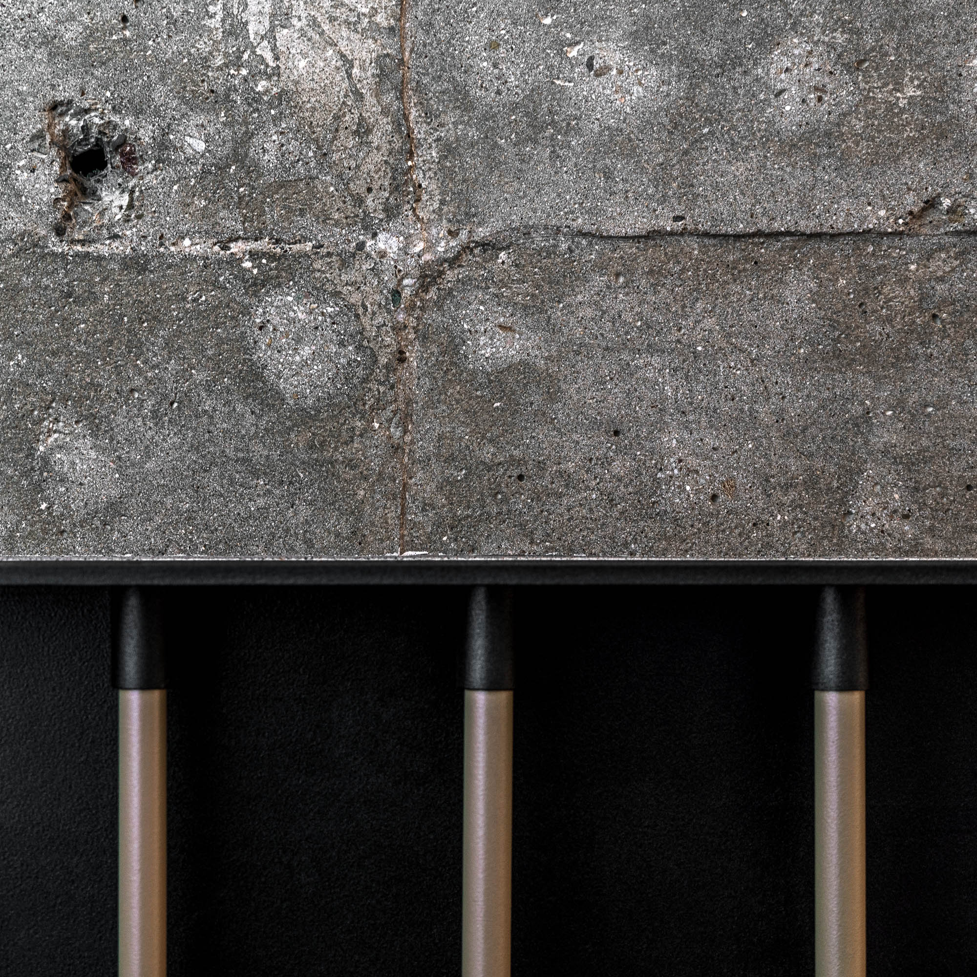 Materiálový detail showroomu LA TABLE Pařížská – přiznané hrubé betonové záhlaví pilíře v kontrastu s tmavou kovovou profilací a mosazným tyčkovým zábradlím – OOOOX