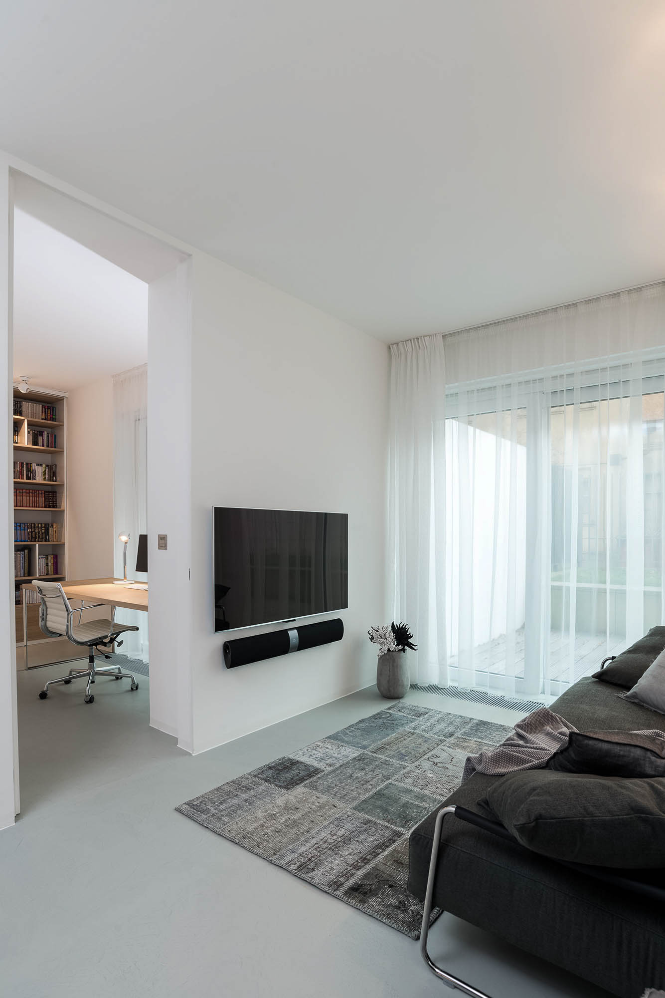 TV koutek s velkou šedou sedačkou – minimalistický interiér bytu od OOOOX