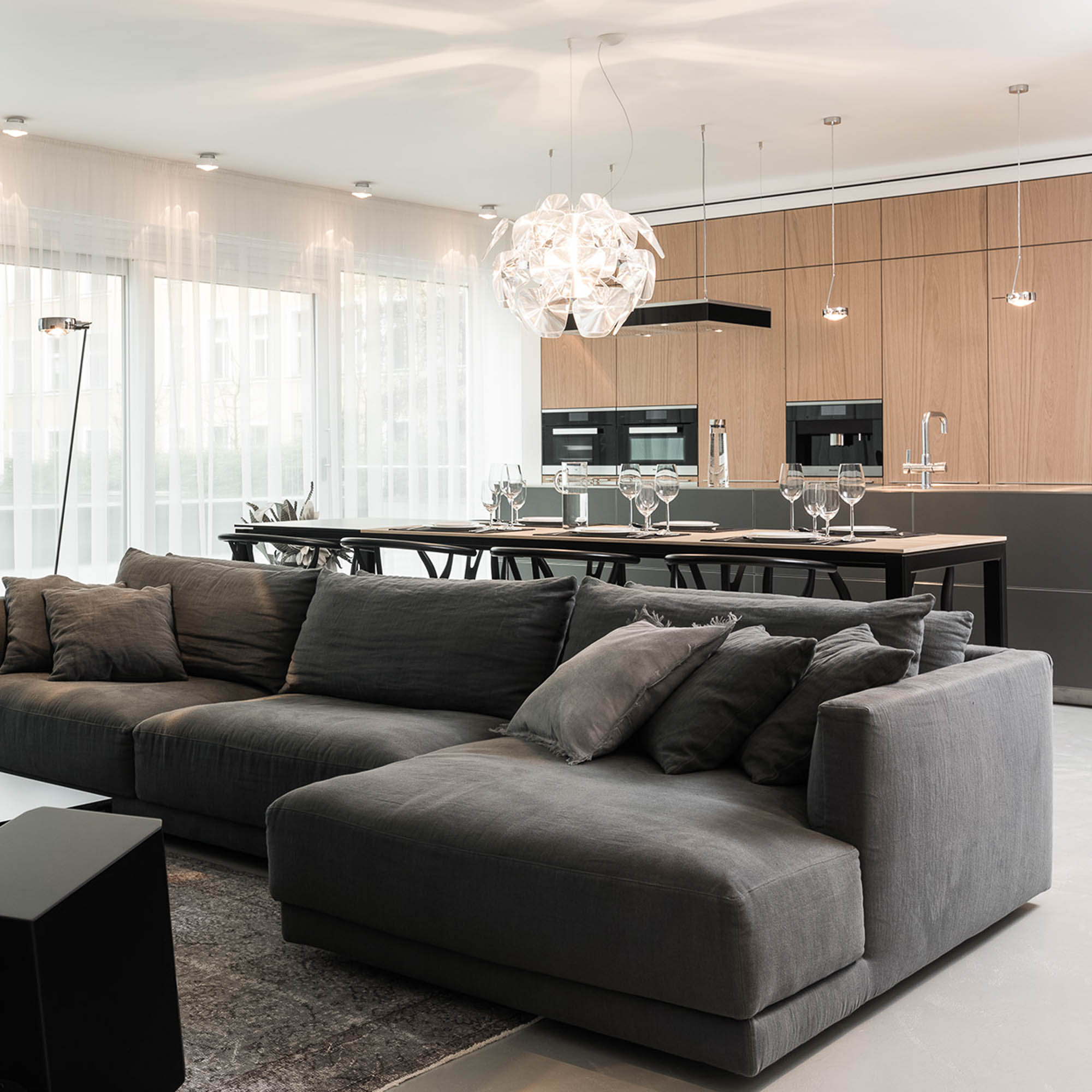 Tmavá sedačka v obývacím pokoji s designovým křeslem – minimalistický interiér | OOOOX