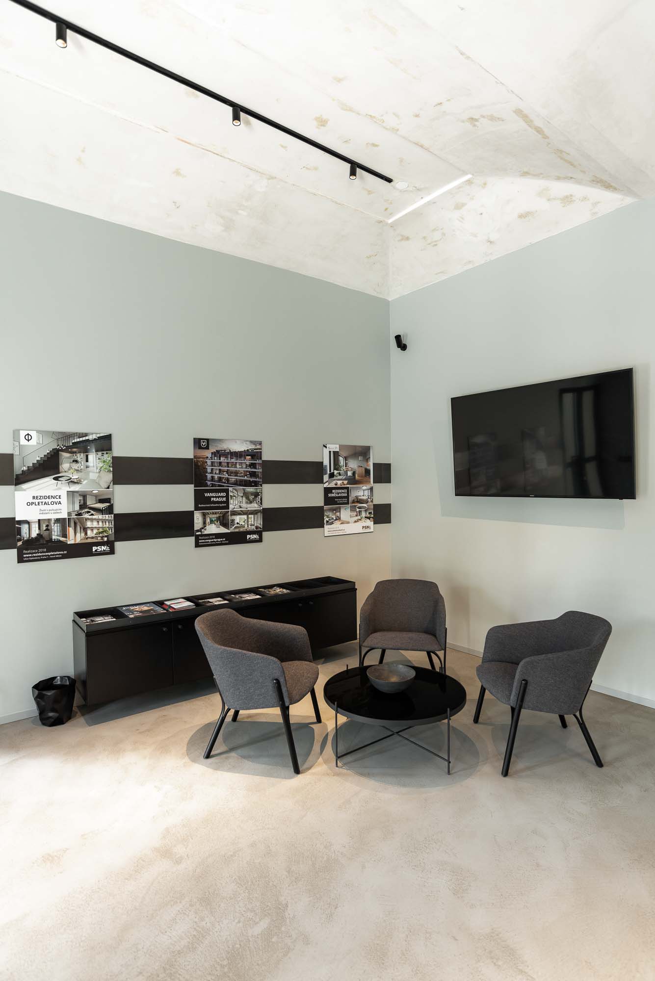 Industriální showroom developerského projektu Vanguard s černými ocelovými prvky, betonovými povrchy, nábytkem na míru a atmosférickým osvětlením v reprezentativních kancelářských prostorách PSN. Design by OOOOX