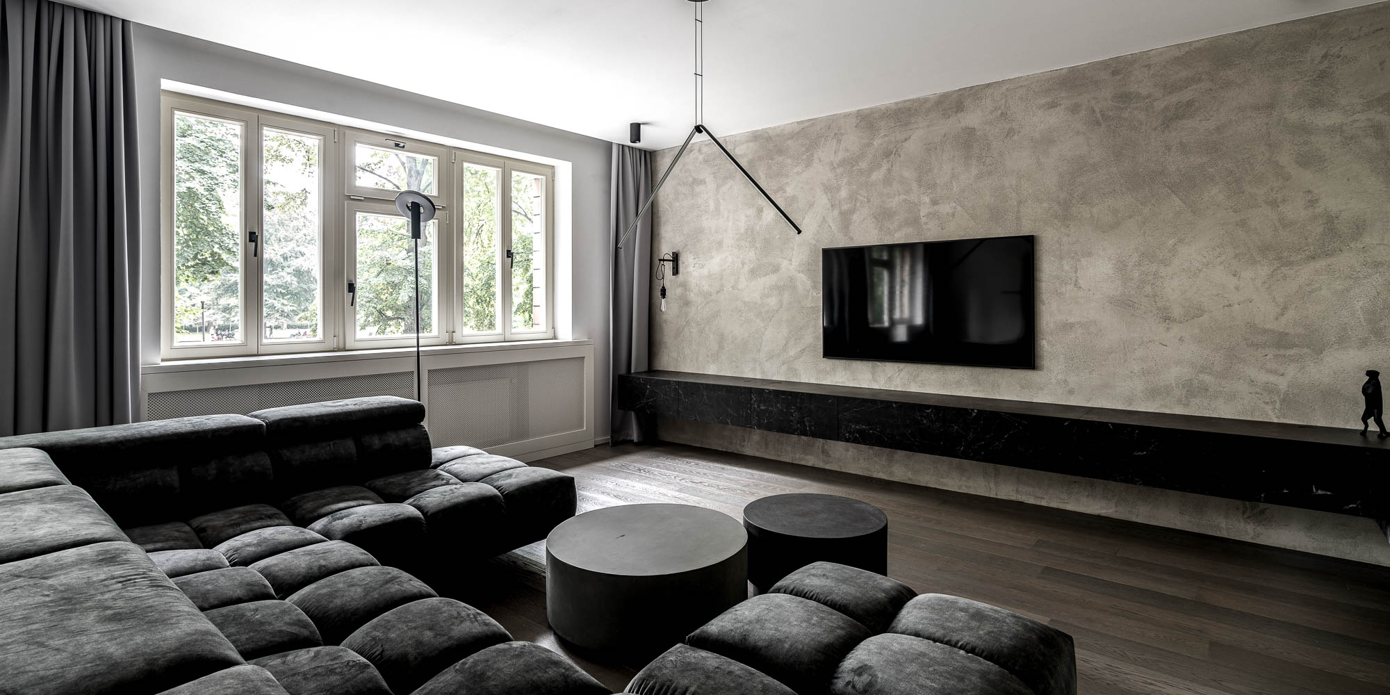Living room with oversized velvet sofa and grey plaster TV wall — apartment renovation Prague OOOOX