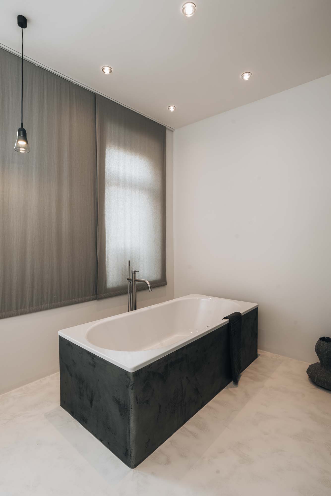 Koupelna s volně stojící vanou, betonovou stěrkou na podlaze, minimalistickou umyvadlovou deskou a syrovými povrchy v industriálním loftovém interiéru. Design by OOOOX