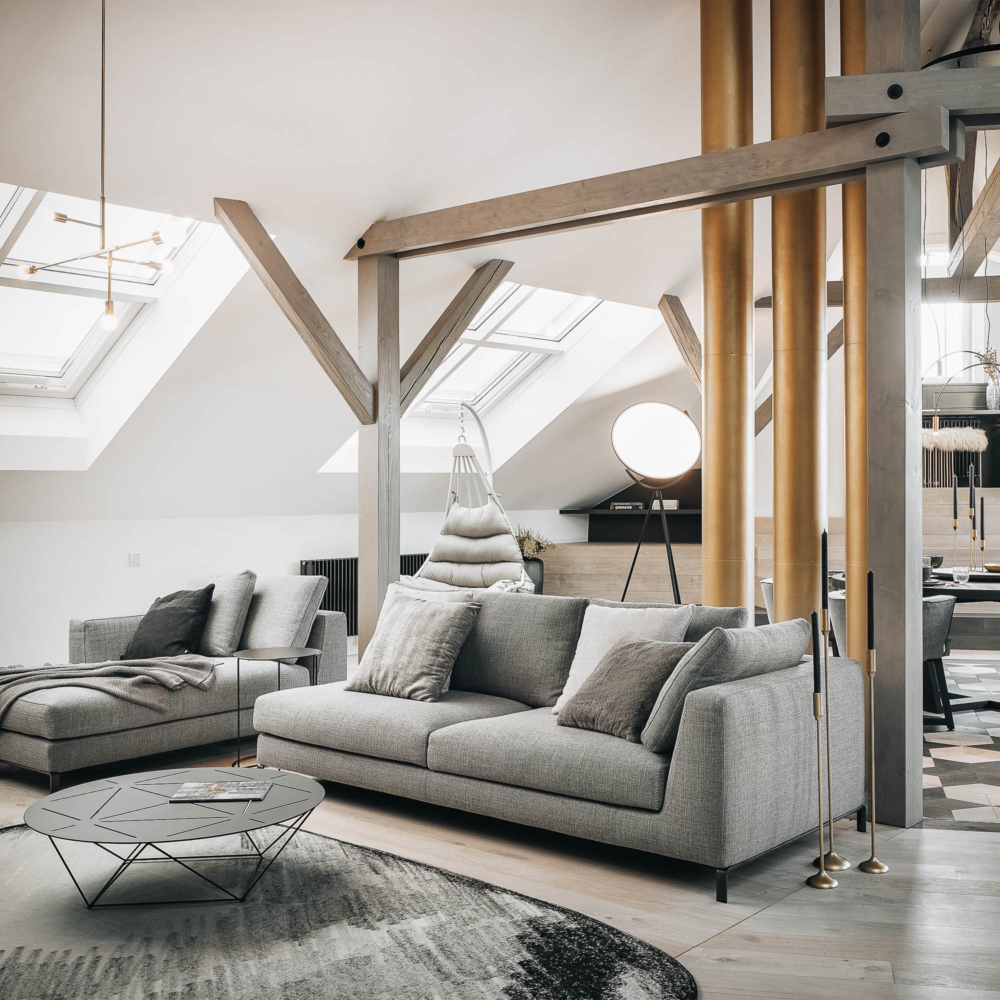 Living room with a grey sofa placed within an attic space featuring exposed chimneys in a brass finish – Josefov reconstruction interior design | OOOOX