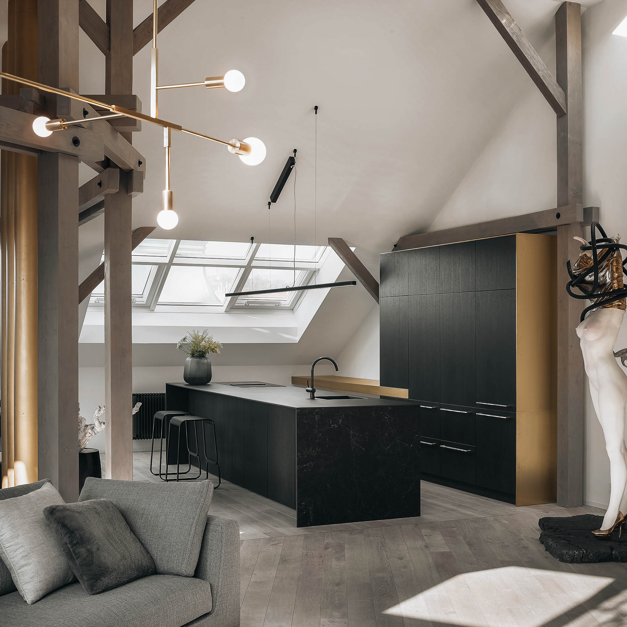 View of black veneer kitchen cabinetry with brass accents, designer pendant light and original roof structure in the Josefov interior reconstruction | OOOOX