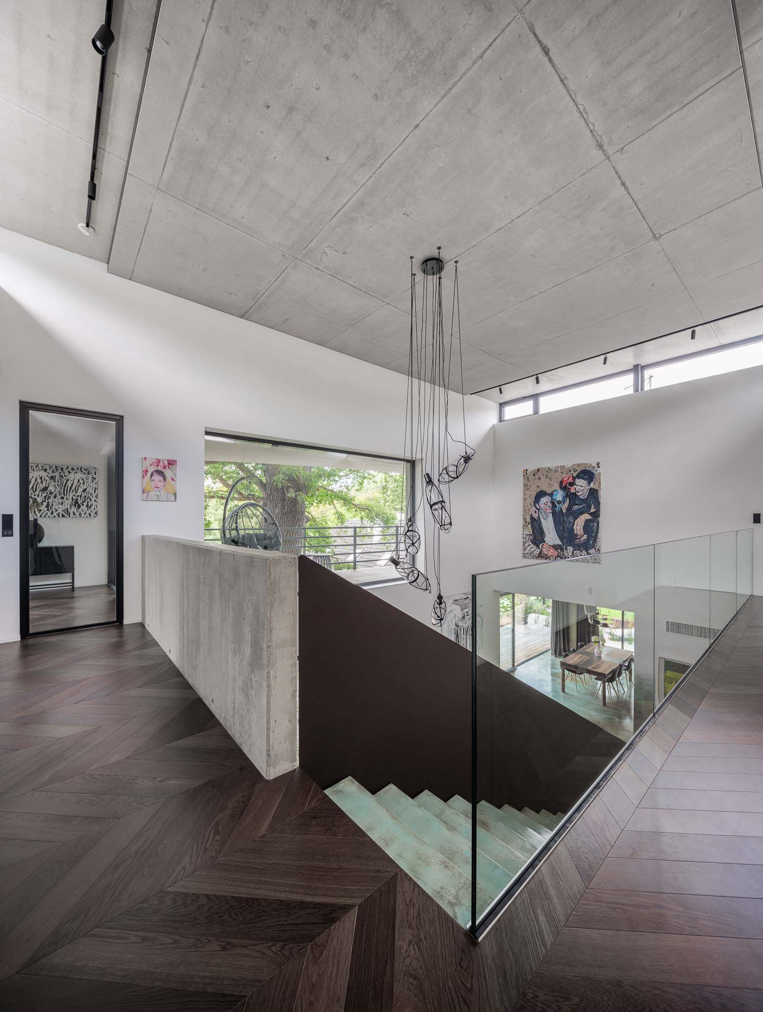 Pohled na otevřený obývací prostor s designovým schodištěm, barevnou stěrkou na podlaze a schodišťových stupních, pohledovým betonem a závěsným svítidlem. Design by OOOOX