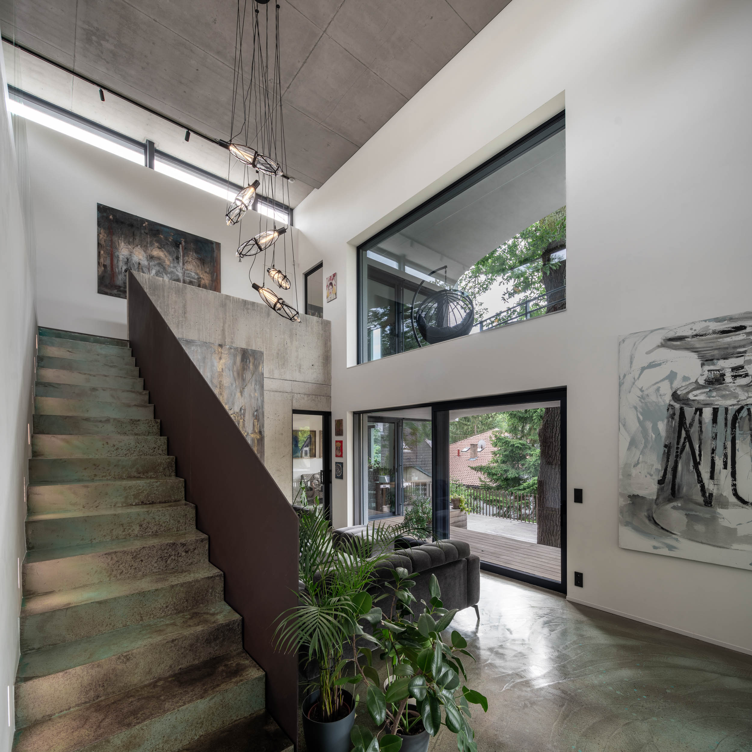 Detail otevřeného obývacího prostoru vily Lučiny se schodištěm opatřeným barevnou stěrkou, designovým svítidlem, tmavou dřevěnou podlahou a pohledovým betonovým stropem. Design by OOOOX