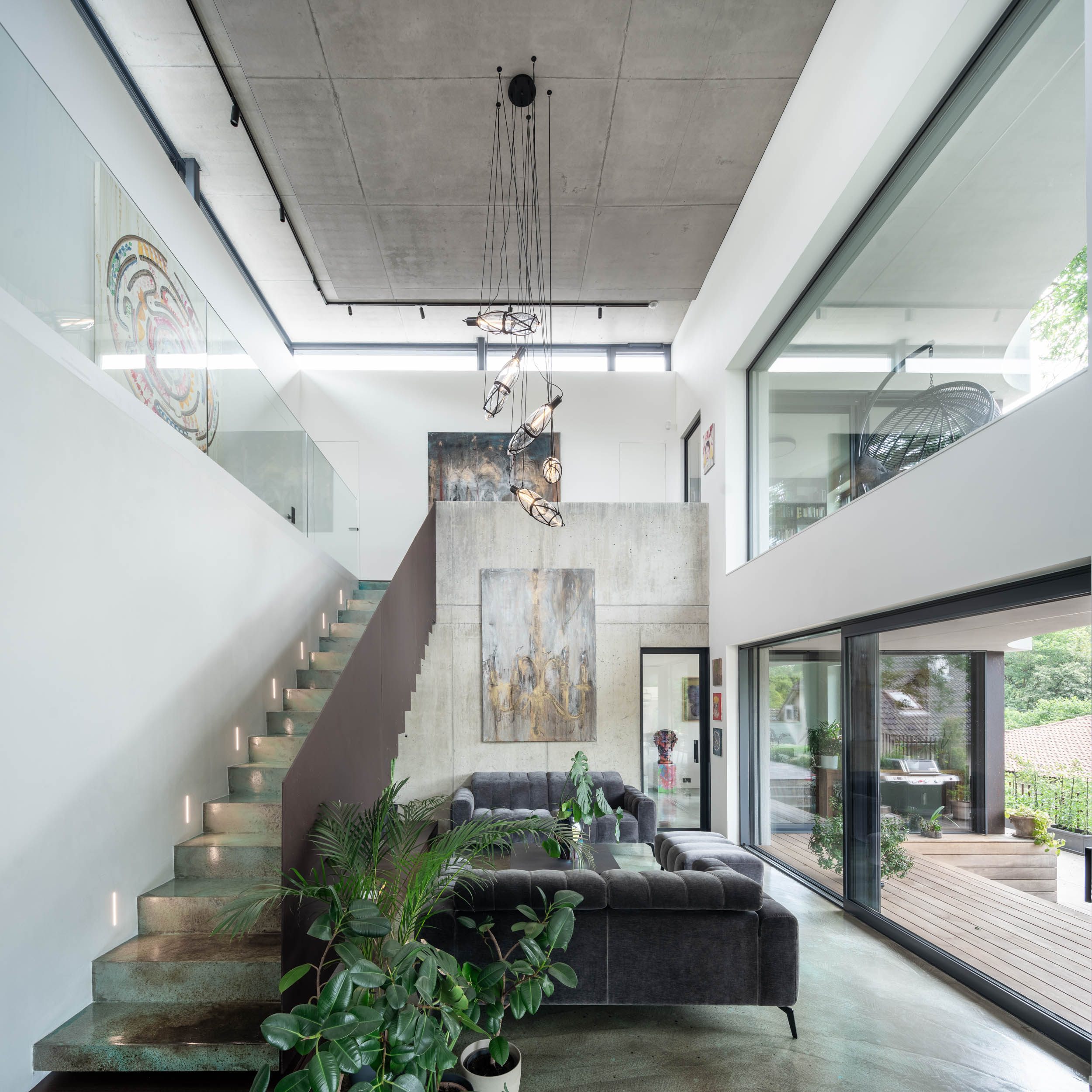 Detail otevřeného obývacího prostoru vily Lučiny se schodištěm opatřeným barevnou stěrkou, designovým svítidlem, tmavou dřevěnou podlahou a pohledovým betonovým stropem. Design by OOOOX
