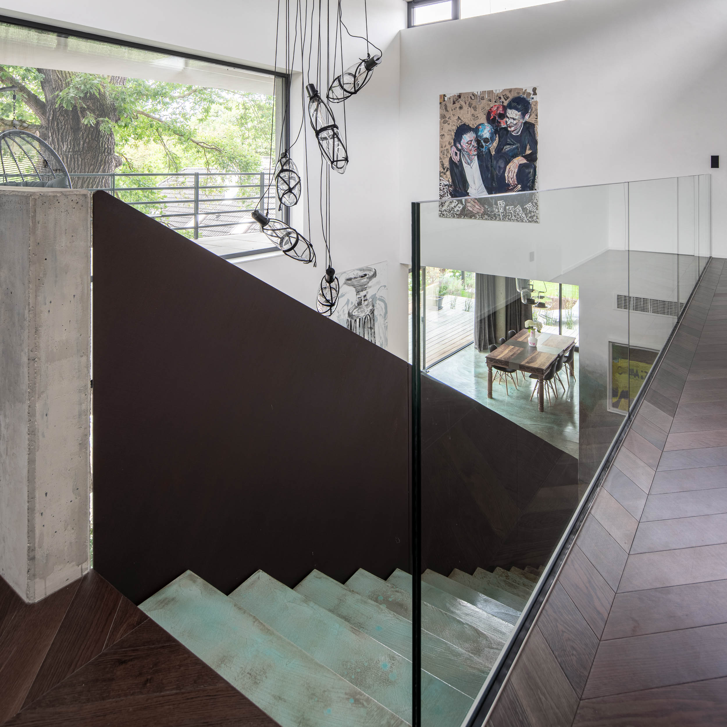 Pohled na otevřený obývací prostor s designovým schodištěm, barevnou stěrkou na podlaze a schodišťových stupních, pohledovým betonem a závěsným svítidlem. Design by OOOOX