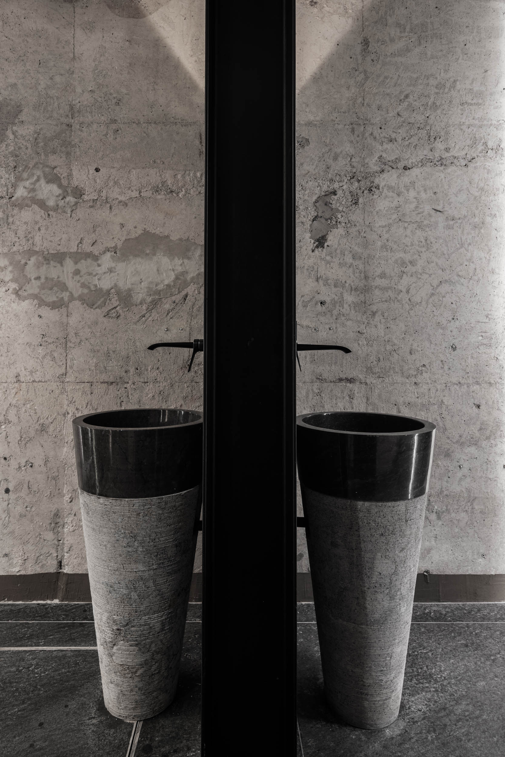 VANGUARD wellness changing room — two symmetrical stone pedestal sinks with black faucets, raw concrete wall, industrial design | OOOOX