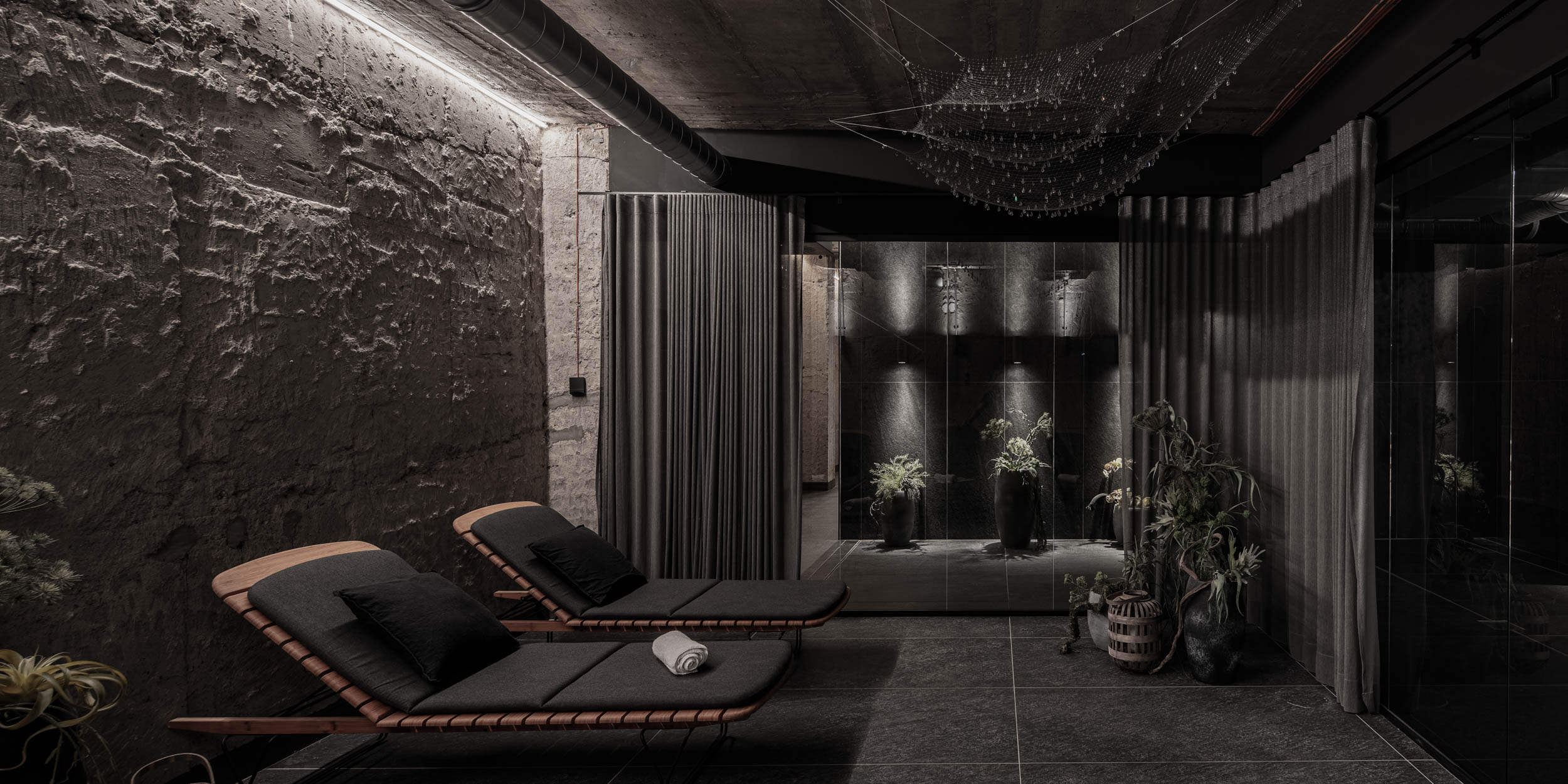 VANGUARD wellness relaxation lounge — dark loungers separated by metal curtains, plant decor, crystal-embellished net ceiling light, glass partition | OOOOX