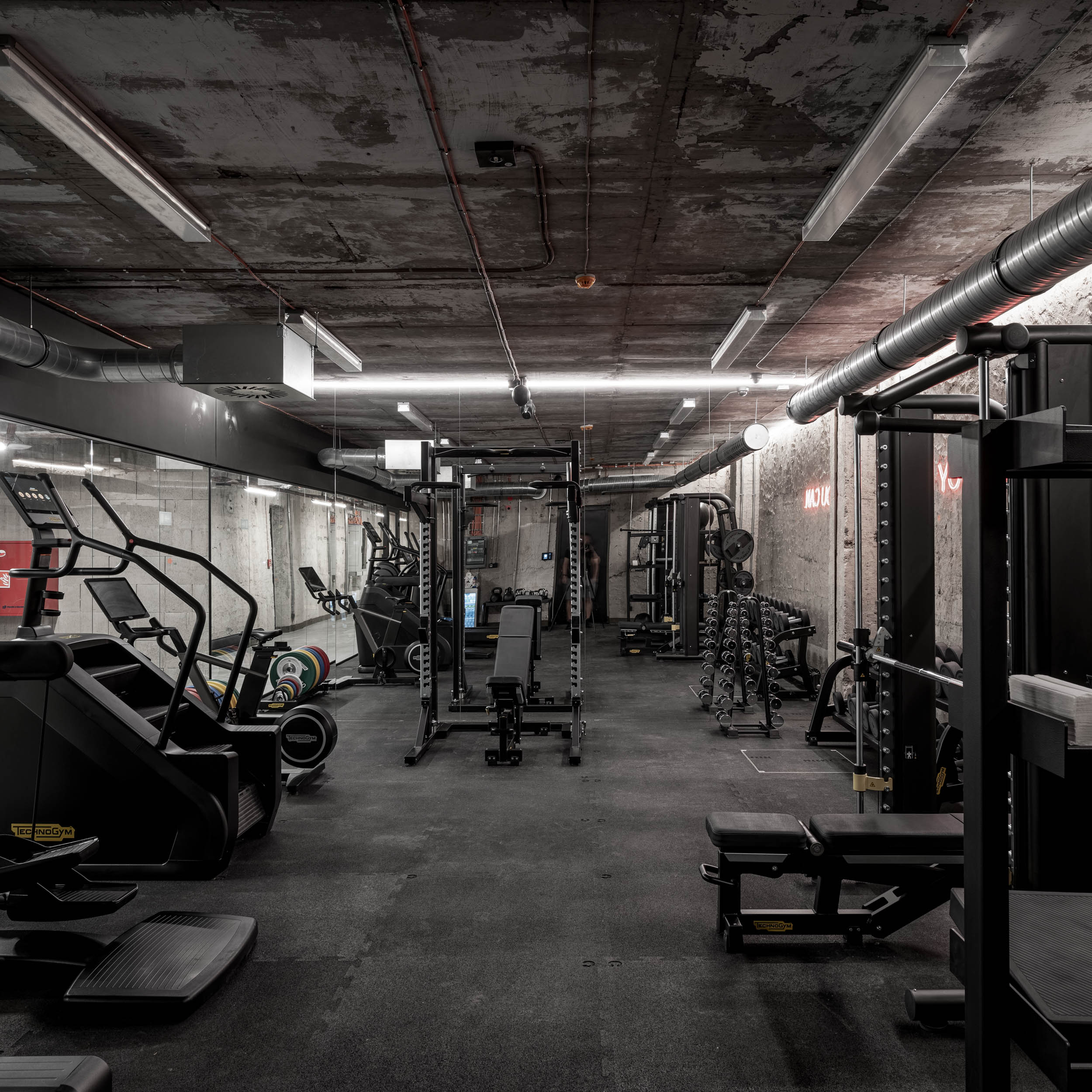 VANGUARD wellness gym — full-length view with cardio machines, weight equipment and mirrors, exposed ductwork, raw concrete ceiling | OOOOX