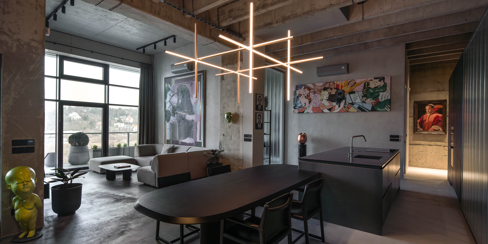 Detail napojení oválného černého jídelního stolu na kuchyňský ostrůvek v minimalistickém industriálním interiéru s designovým závěsným svítidlem. Design by OOOOX