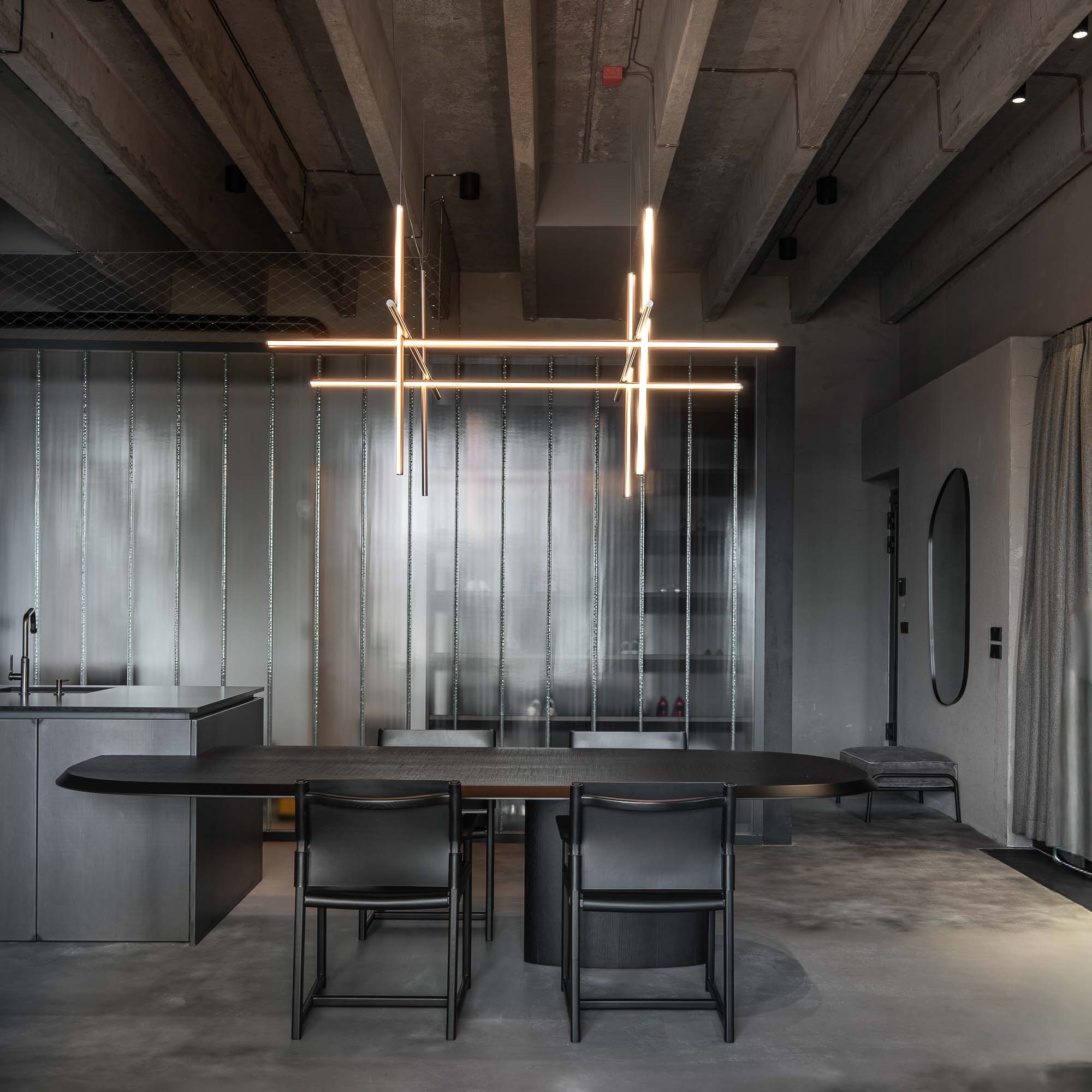 Detail napojení oválného černého jídelního stolu na kuchyňský ostrůvek v minimalistickém industriálním interiéru s designovým závěsným svítidlem. Design by OOOOX