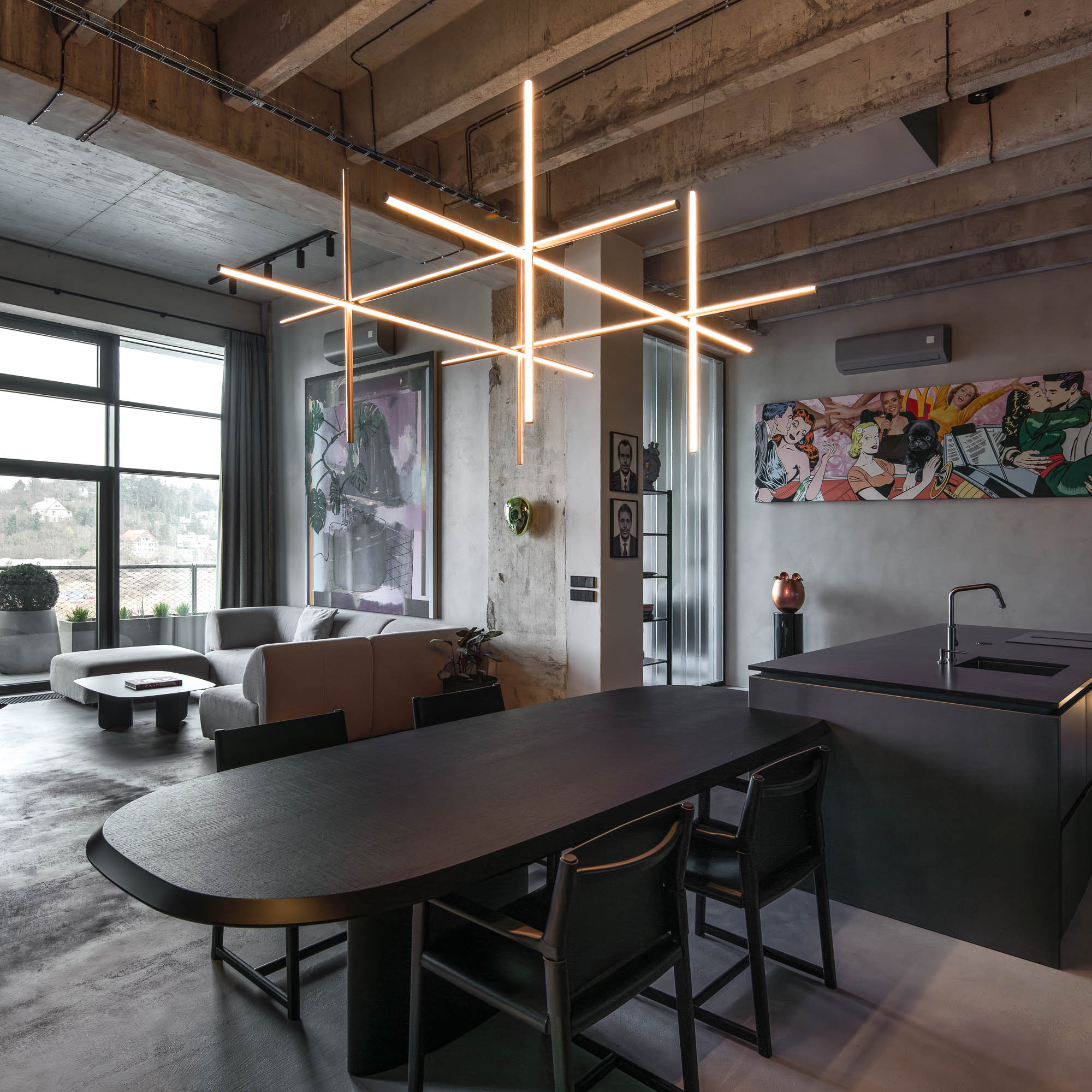 Detail napojení oválného černého jídelního stolu na kuchyňský ostrůvek v minimalistickém industriálním interiéru s designovým závěsným svítidlem. Design by OOOOX
