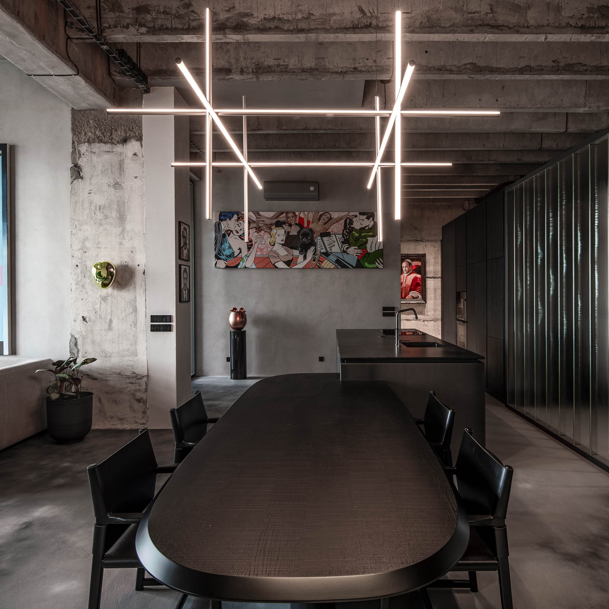 Detail napojení oválného černého jídelního stolu na kuchyňský ostrůvek v minimalistickém industriálním interiéru s designovým závěsným svítidlem. Design by OOOOX