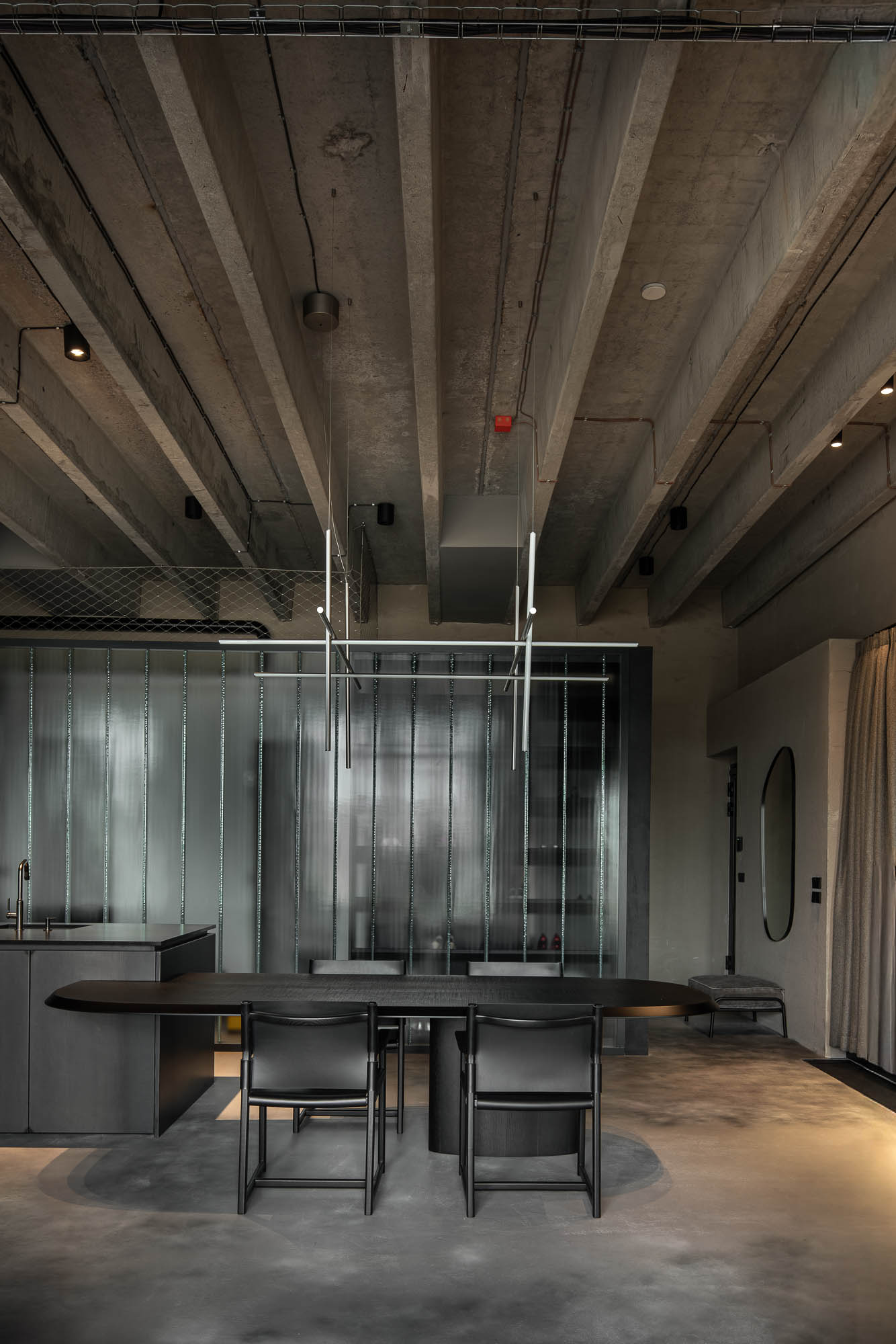 Detail napojení oválného černého jídelního stolu na kuchyňský ostrůvek v minimalistickém industriálním interiéru s designovým závěsným svítidlem. Design by OOOOX