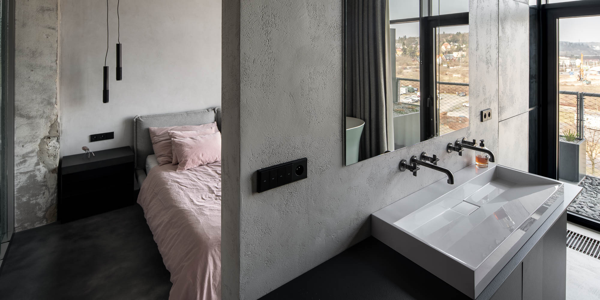 Detail propojení ložnice a koupelny s volně stojící vanou a výhledem na Prahu v otevřeném loftovém interiéru. Design by OOOOX