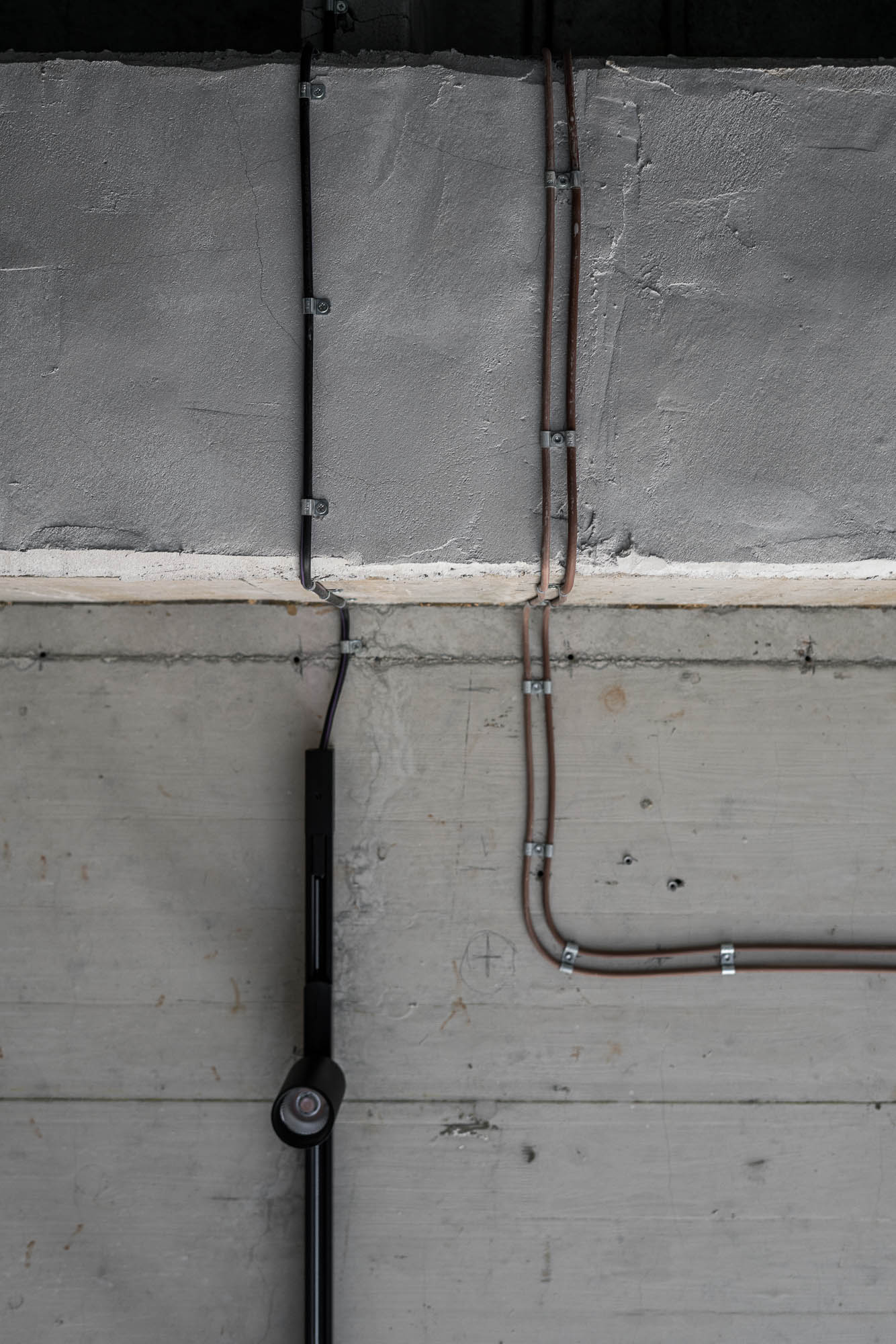 Detail kabelu vedeného po syrové betonové stěně v minimalistickém industriálním interiéru loftového bytu Vanguard. Design by OOOOX
