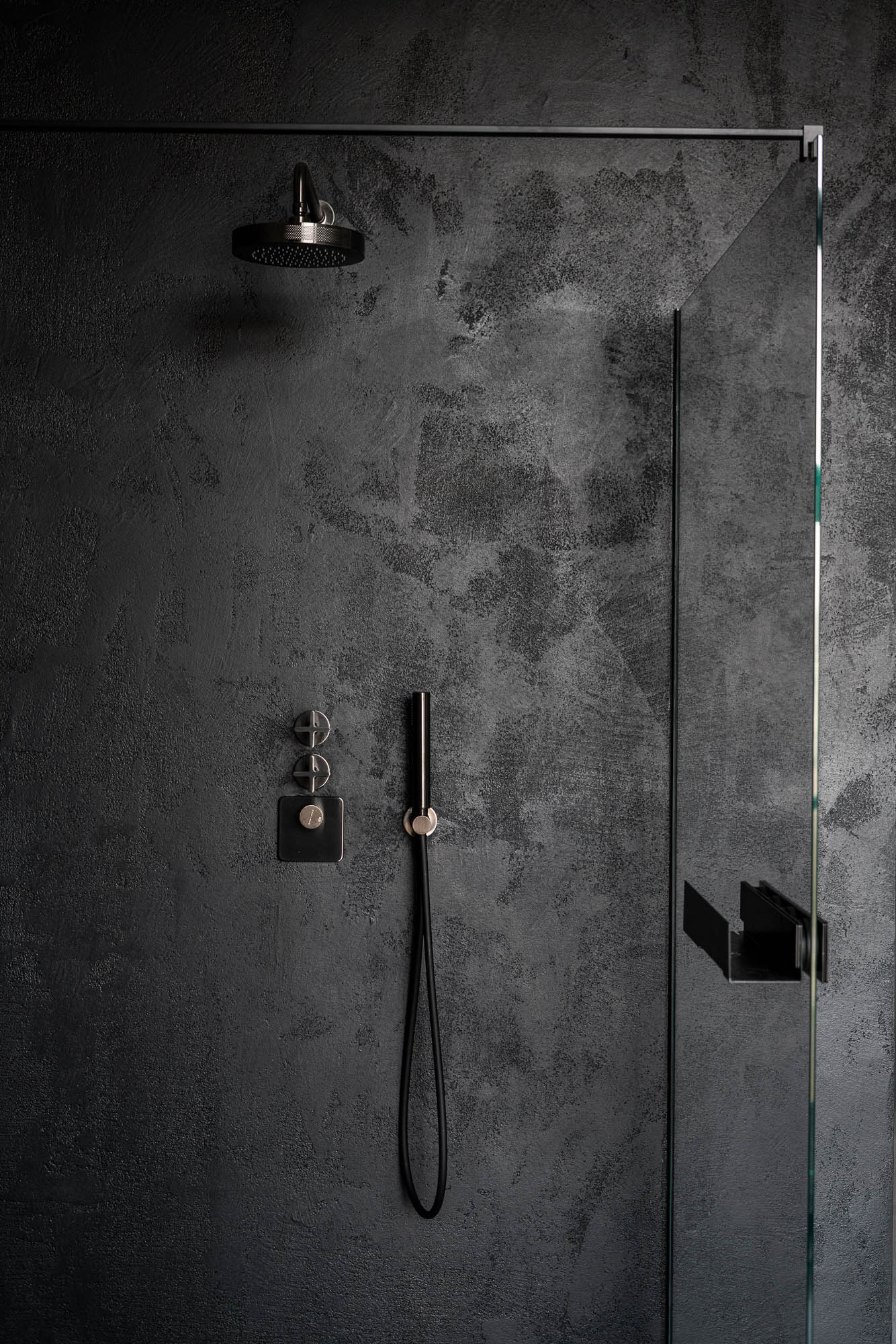 Detail of black concrete wall finish inside the shower enclosure of a minimalist industrial loft bathroom. Design by OOOOX