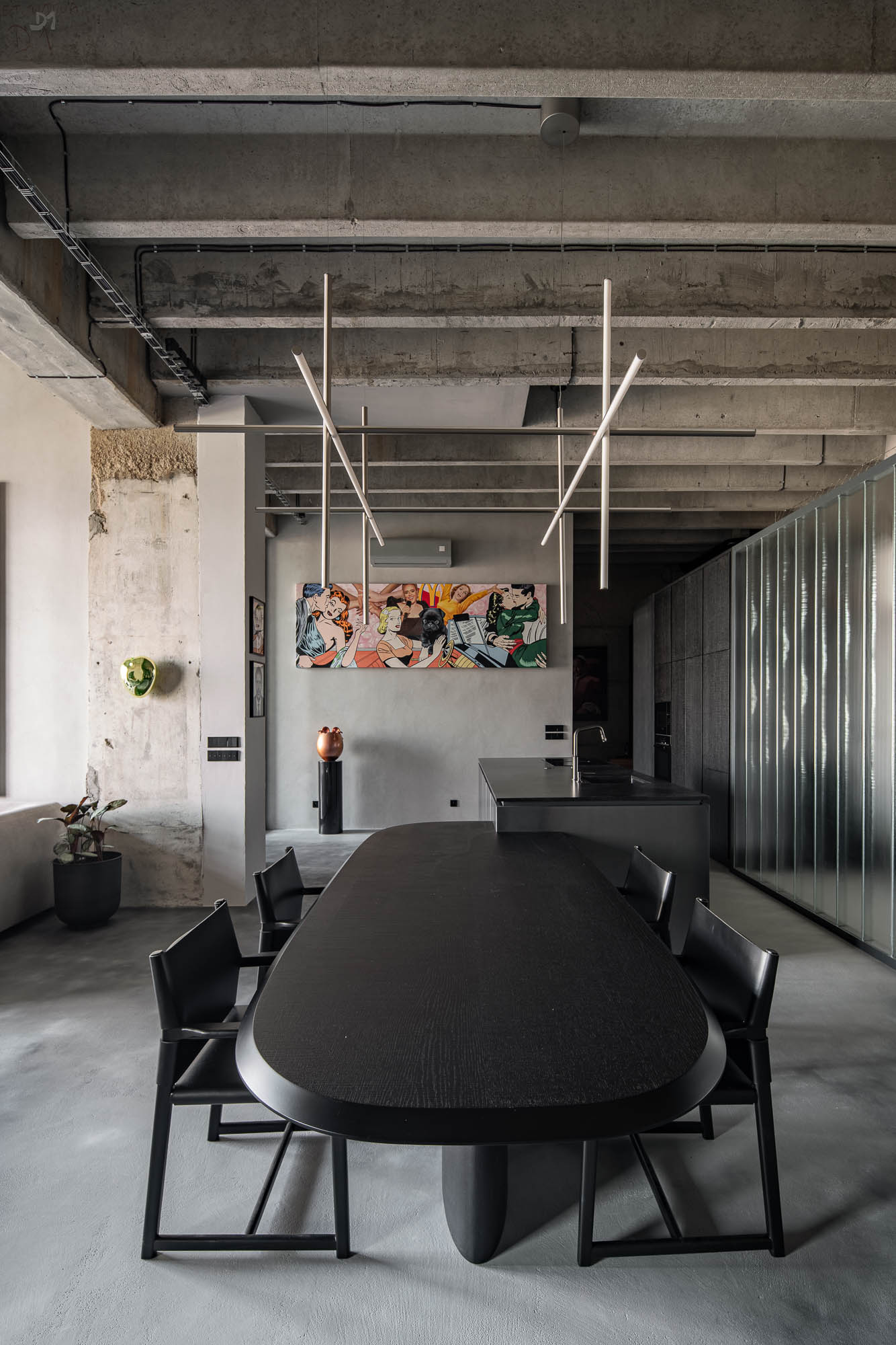 Detail napojení oválného černého jídelního stolu na kuchyňský ostrůvek v minimalistickém industriálním interiéru s designovým závěsným svítidlem. Design by OOOOX