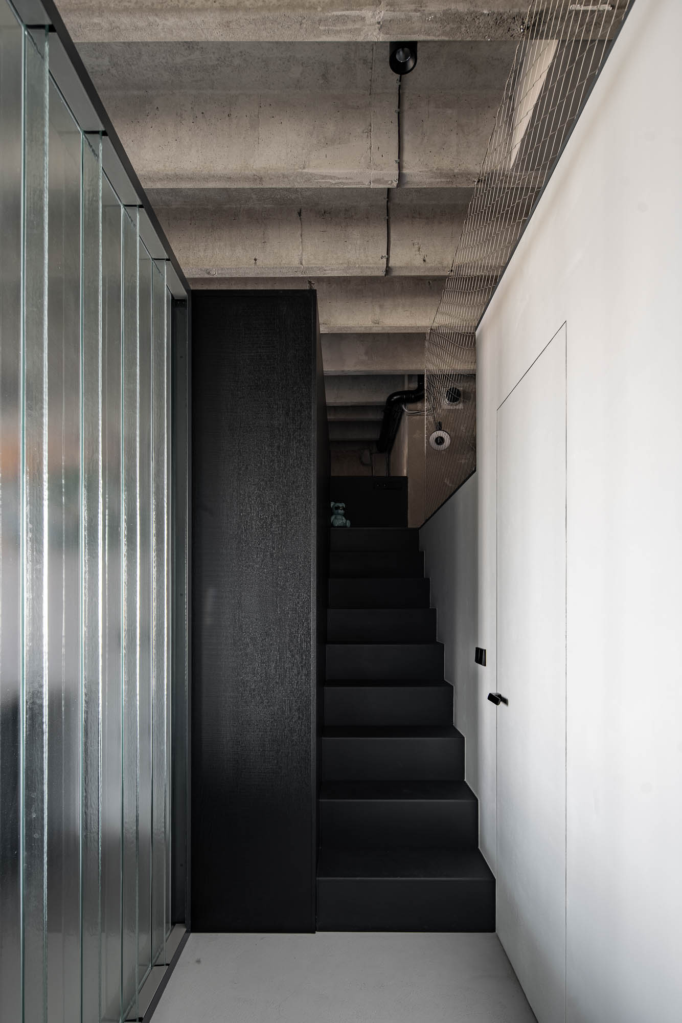 Detail of a private corridor separated by a copilit partition, concrete flooring, built-in furniture and staircase leading to the upper guest sleeping area. Design by OOOOX