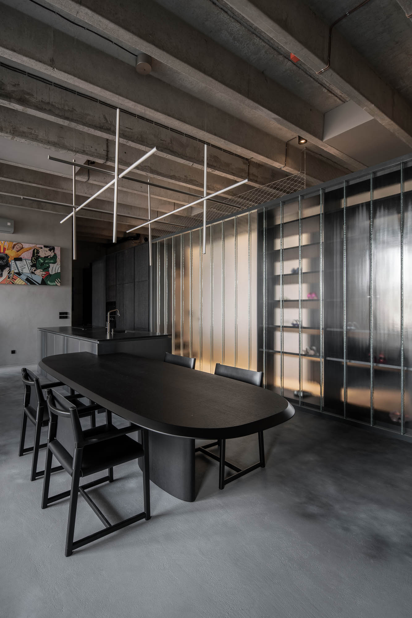 Detail napojení oválného černého jídelního stolu na kuchyňský ostrůvek v minimalistickém industriálním interiéru s designovým závěsným svítidlem. Design by OOOOX
