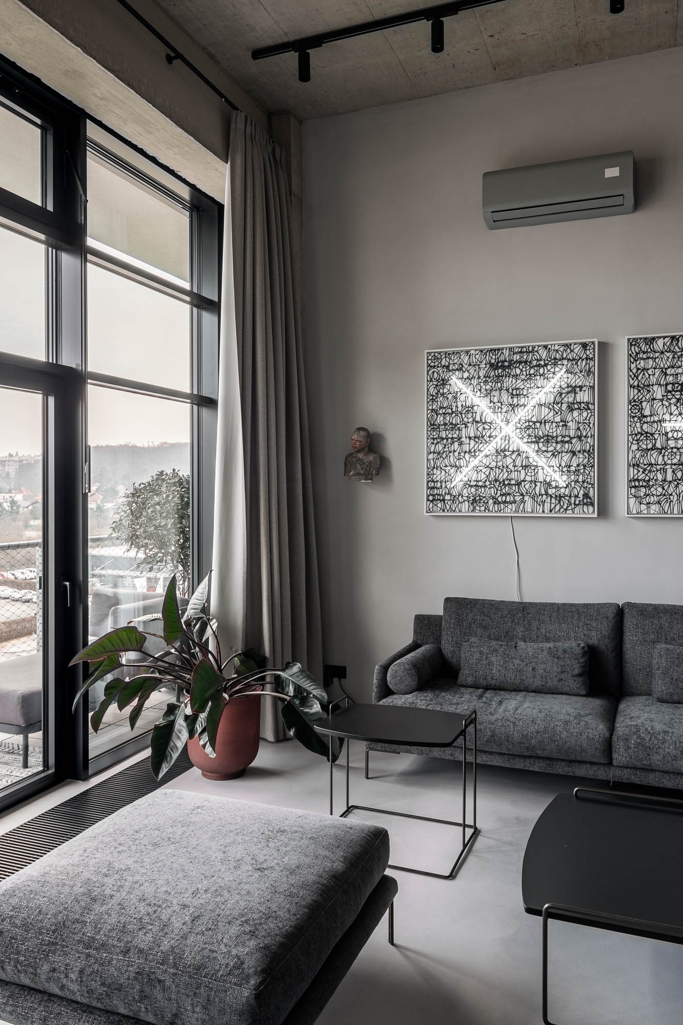 Rohový pohled na obývací prostor loftu Vanguard s šedou sedačkou, panoramatickým oknem s výhledem na město a neonovým uměleckým dílem na zdi – OOOOX