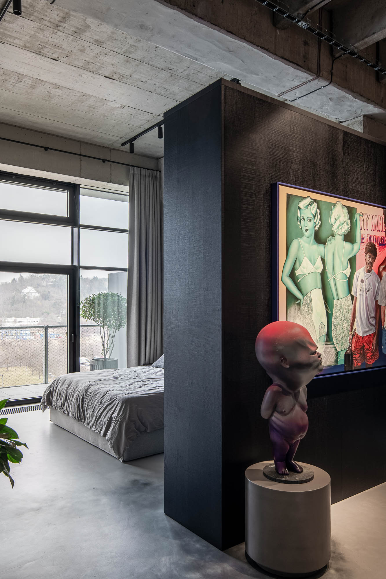 Přechod do ložnicové části loftu Vanguard – tmavý textilní dělící prvek, barevná pop-art malba a figurální soška na betonové podlaze – OOOOX design