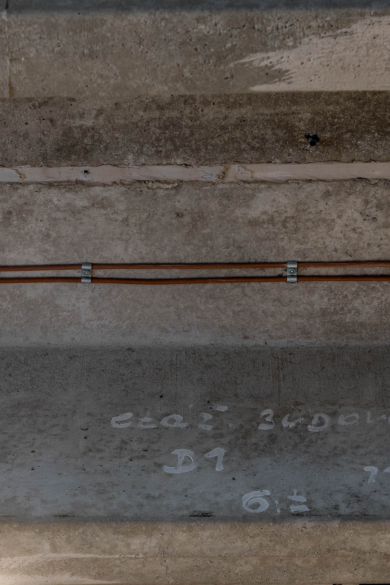 Detail přiznaného betonového sloupu s původními křídovými stavebními značkami a měděným potrubím – autentická průmyslová architektura loftu Vanguard OOOOX