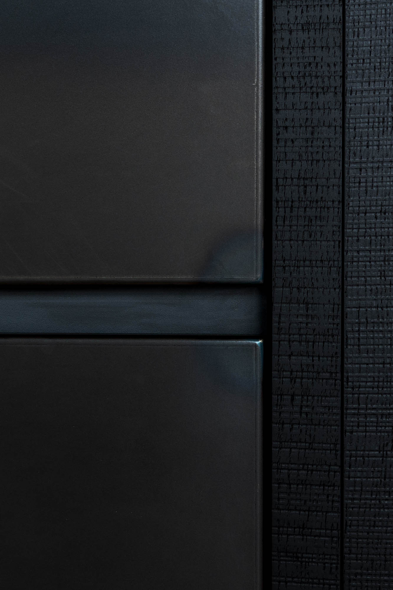 Materiálový detail loftu Vanguard – kontrast černých matných kuchyňských dvířek a tmavého tkaného textilního povrchu nábytkového bloku – OOOOX design