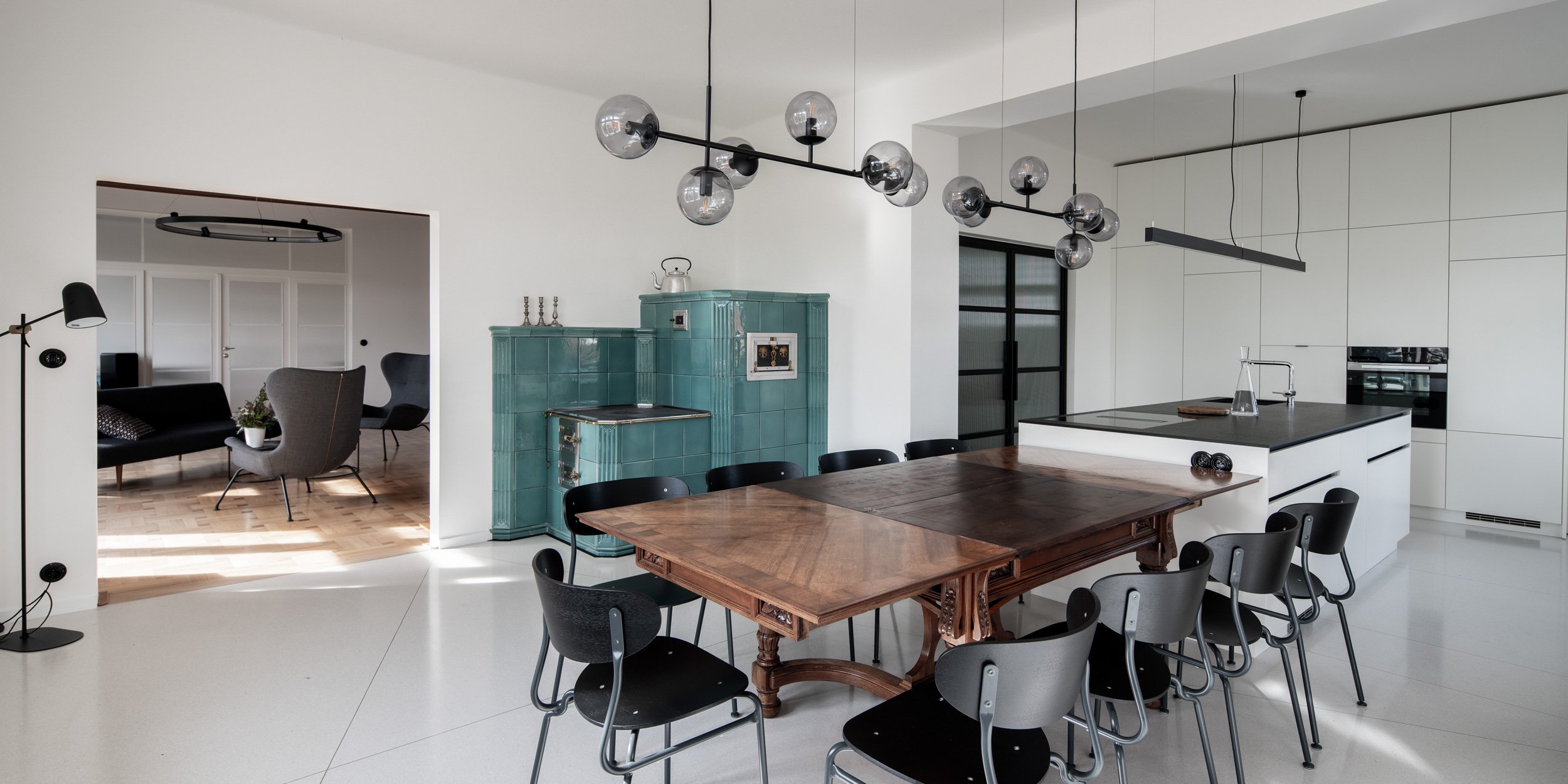Dining room with kitchen – panorama including view into living room on left, turquoise tiled stove, carved dining table, kitchen island, ribbed glass door on right. OOOOX